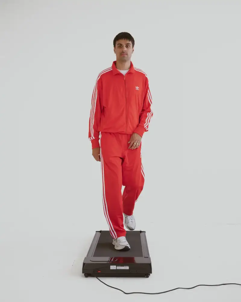 HOW SHAI DATAUKER REDEFINES CLOTHING, IDENTITY, AND DAILY LIFE Shai Datauker wearing his daily uniform-a bright red Adidas tracksuit and white t-shirt-sitting in a minimalist interior during an interview about fashion and identity. (image 2 of 5)