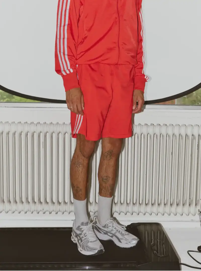 HOW SHAI DATAUKER REDEFINES CLOTHING, IDENTITY, AND DAILY LIFE Shai Datauker wearing his daily uniform-a bright red Adidas tracksuit and white t-shirt-sitting in a minimalist interior during an interview about fashion and identity. (image 3 of 5)