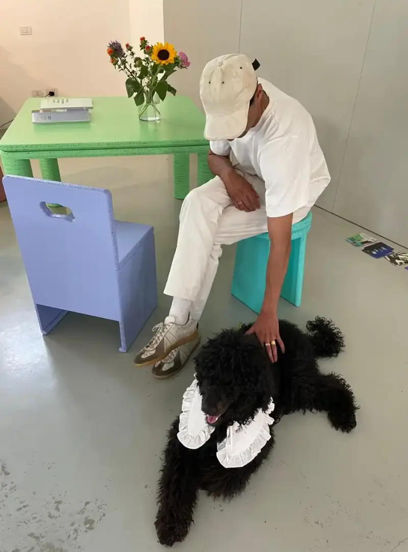 HOW SHAI DATAUKER REDEFINES CLOTHING, IDENTITY, AND DAILY LIFE Shai Datauker wearing his daily uniform-a bright red Adidas tracksuit and white t-shirt-sitting in a minimalist interior during an interview about fashion and identity. (image 3 of 4)