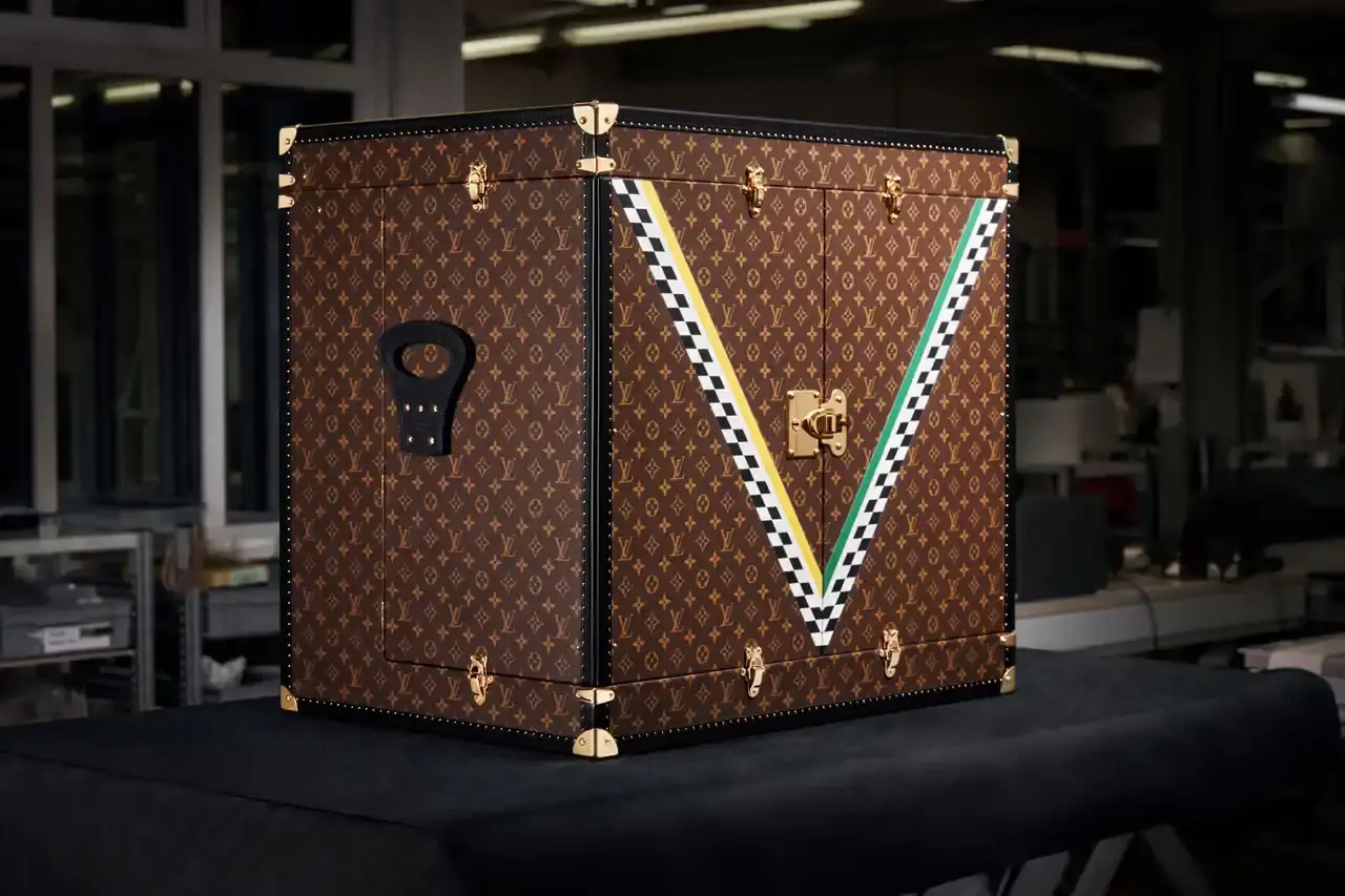 Louis Vuitton/Formula 1 A Louis Vuitton trophy trunk with classic brown monogram pattern and gold accents. The trunk features diagonal green and gold checkerboard details on its doors, representing Australian national colors. When opened, it displays a Formula 1 steering wheel centerpiece. The trunk combines Louis Vuitton's luxury heritage with motorsport elements for the 2025 Australian Grand Prix. (image 3 of 3)