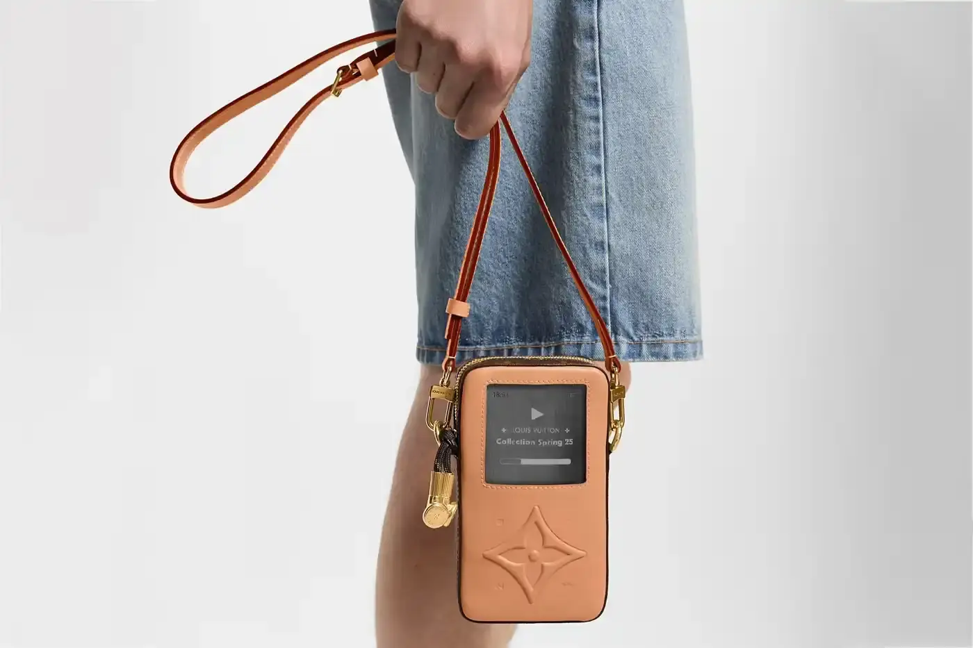 Louis Vuitton Louis Vuitton Spring 2025 accessories collection featuring music technology-inspired luxury items. The image shows an iPod-shaped leather crossbody bag with a display screen showing 'Louis Vuitton Collection Spring 2025' and an LV monogram replacing the scroll wheel. Also visible are a cassette player-styled wallet with embossed control buttons and a cassette tape card holder with 'Side A' and 'Side B' graphics. Gold headphone-shaped zipper pulls complete the nostalgic design. (image 2 of 17)