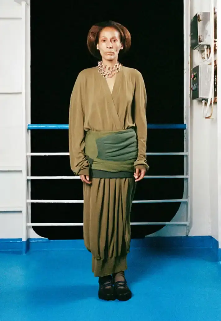 MAGLIANO SHOWS SS26 COLLECTION VIA FERRY FILM image about Italian designer Luca Magliano's Spring/Summer 2026 menswear collection, presented as a film aboard a ferry during Milan Fashion Week. The collection features camping and nomadic influences, with repurposed materials, loose silhouettes, and collaborative footwear including Beja soccer sneakers and 1900s-inspired boots. Shoot by Leonardo Scotti. (image 15 of 16)