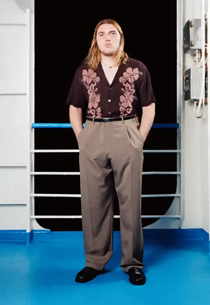 MAGLIANO SHOWS SS26 COLLECTION VIA FERRY FILM image about Italian designer Luca Magliano's Spring/Summer 2026 menswear collection, presented as a film aboard a ferry during Milan Fashion Week. The collection features camping and nomadic influences, with repurposed materials, loose silhouettes, and collaborative footwear including Beja soccer sneakers and 1900s-inspired boots. Shoot by Leonardo Scotti. (image 10 of 16)