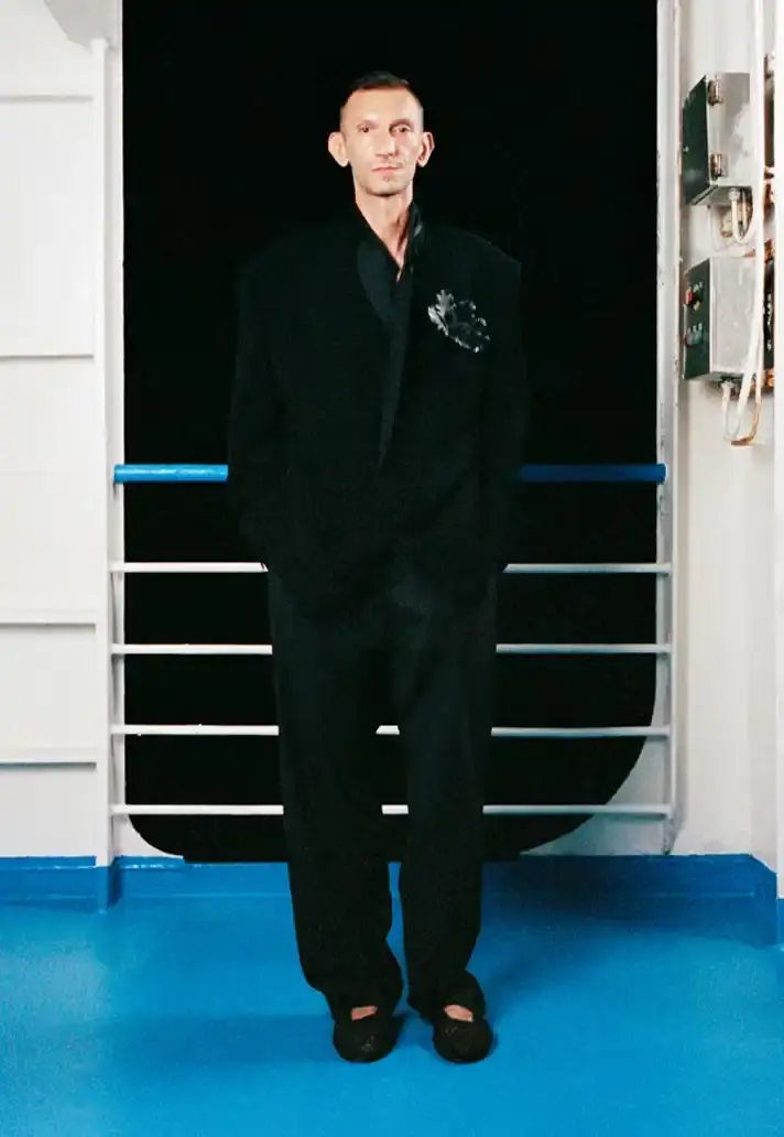 MAGLIANO SHOWS SS26 COLLECTION VIA FERRY FILM image about Italian designer Luca Magliano's Spring/Summer 2026 menswear collection, presented as a film aboard a ferry during Milan Fashion Week. The collection features camping and nomadic influences, with repurposed materials, loose silhouettes, and collaborative footwear including Beja soccer sneakers and 1900s-inspired boots. Shoot by Leonardo Scotti. (image 9 of 16)