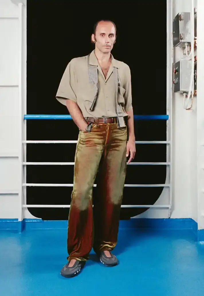 MAGLIANO SHOWS SS26 COLLECTION VIA FERRY FILM image about Italian designer Luca Magliano's Spring/Summer 2026 menswear collection, presented as a film aboard a ferry during Milan Fashion Week. The collection features camping and nomadic influences, with repurposed materials, loose silhouettes, and collaborative footwear including Beja soccer sneakers and 1900s-inspired boots. Shoot by Leonardo Scotti. (image 11 of 16)