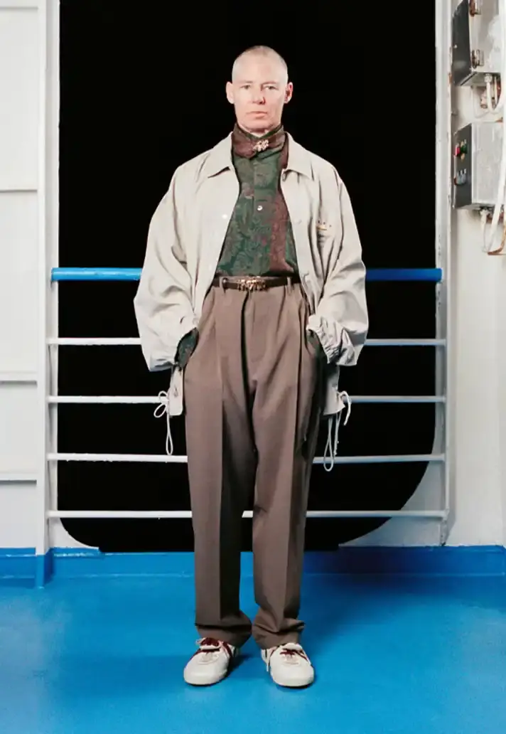 MAGLIANO SHOWS SS26 COLLECTION VIA FERRY FILM image about Italian designer Luca Magliano's Spring/Summer 2026 menswear collection, presented as a film aboard a ferry during Milan Fashion Week. The collection features camping and nomadic influences, with repurposed materials, loose silhouettes, and collaborative footwear including Beja soccer sneakers and 1900s-inspired boots. Shoot by Leonardo Scotti. (image 3 of 16)