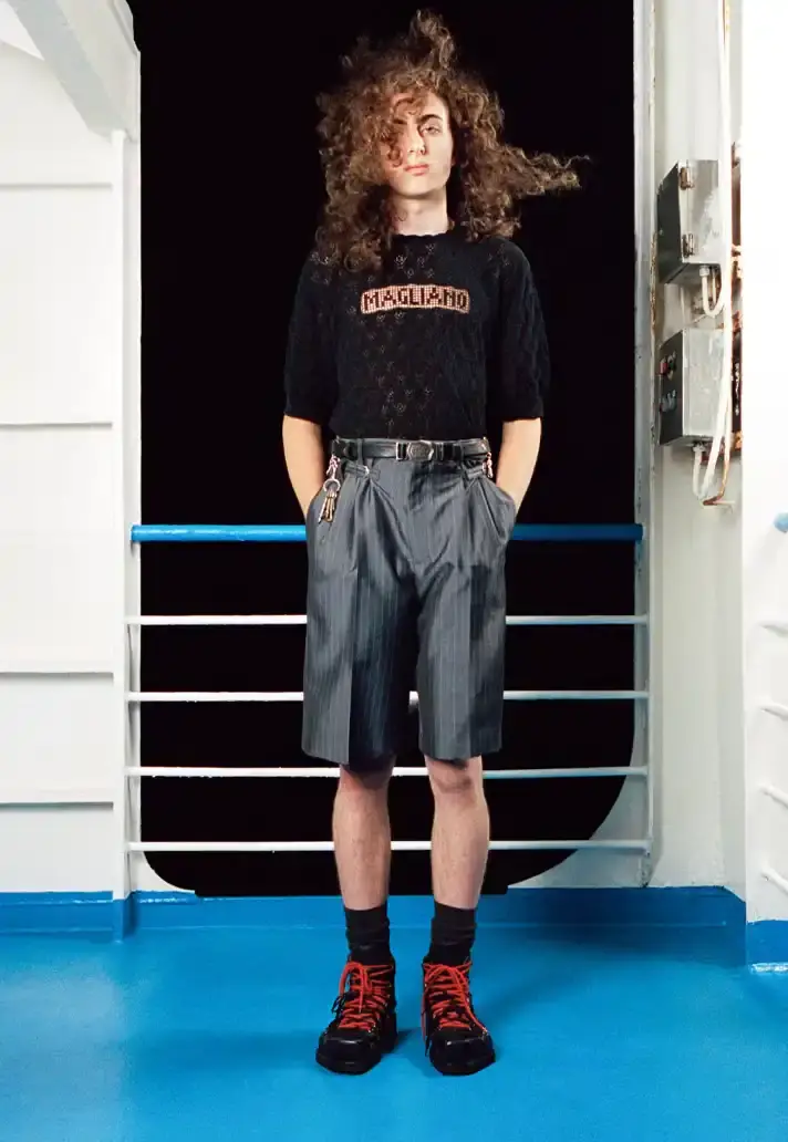 MAGLIANO SHOWS SS26 COLLECTION VIA FERRY FILM image about Italian designer Luca Magliano's Spring/Summer 2026 menswear collection, presented as a film aboard a ferry during Milan Fashion Week. The collection features camping and nomadic influences, with repurposed materials, loose silhouettes, and collaborative footwear including Beja soccer sneakers and 1900s-inspired boots. Shoot by Leonardo Scotti. (image 12 of 16)