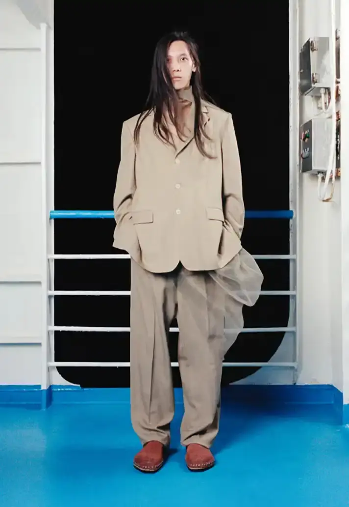 MAGLIANO SHOWS SS26 COLLECTION VIA FERRY FILM image about Italian designer Luca Magliano's Spring/Summer 2026 menswear collection, presented as a film aboard a ferry during Milan Fashion Week. The collection features camping and nomadic influences, with repurposed materials, loose silhouettes, and collaborative footwear including Beja soccer sneakers and 1900s-inspired boots. Shoot by Leonardo Scotti. (image 4 of 16)