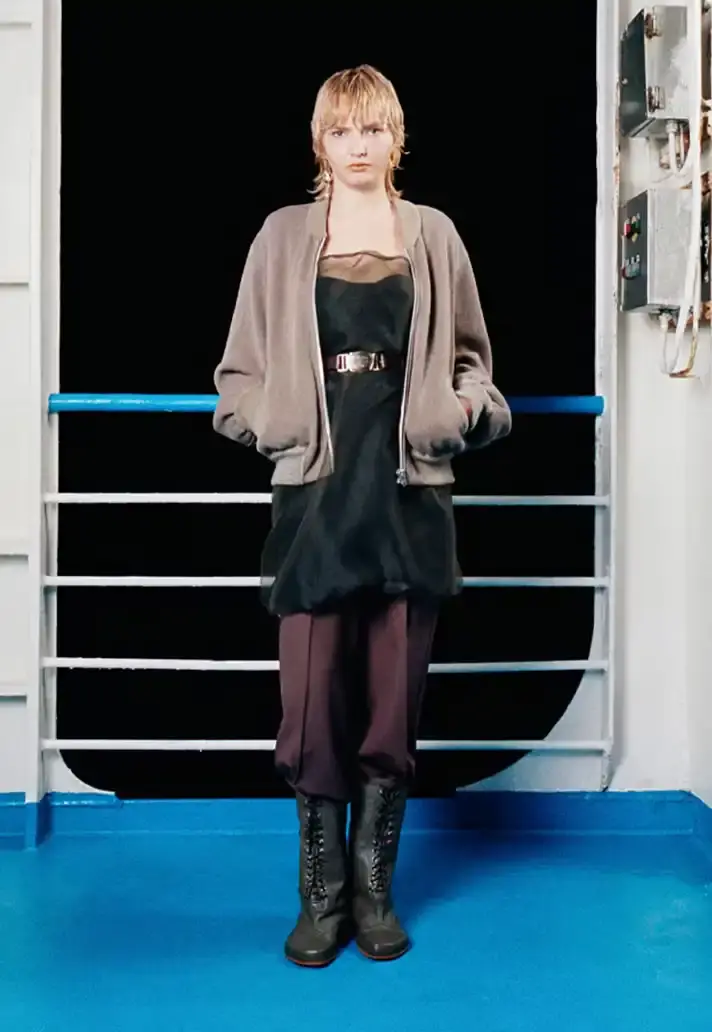 MAGLIANO SHOWS SS26 COLLECTION VIA FERRY FILM image about Italian designer Luca Magliano's Spring/Summer 2026 menswear collection, presented as a film aboard a ferry during Milan Fashion Week. The collection features camping and nomadic influences, with repurposed materials, loose silhouettes, and collaborative footwear including Beja soccer sneakers and 1900s-inspired boots. Shoot by Leonardo Scotti. (image 5 of 16)