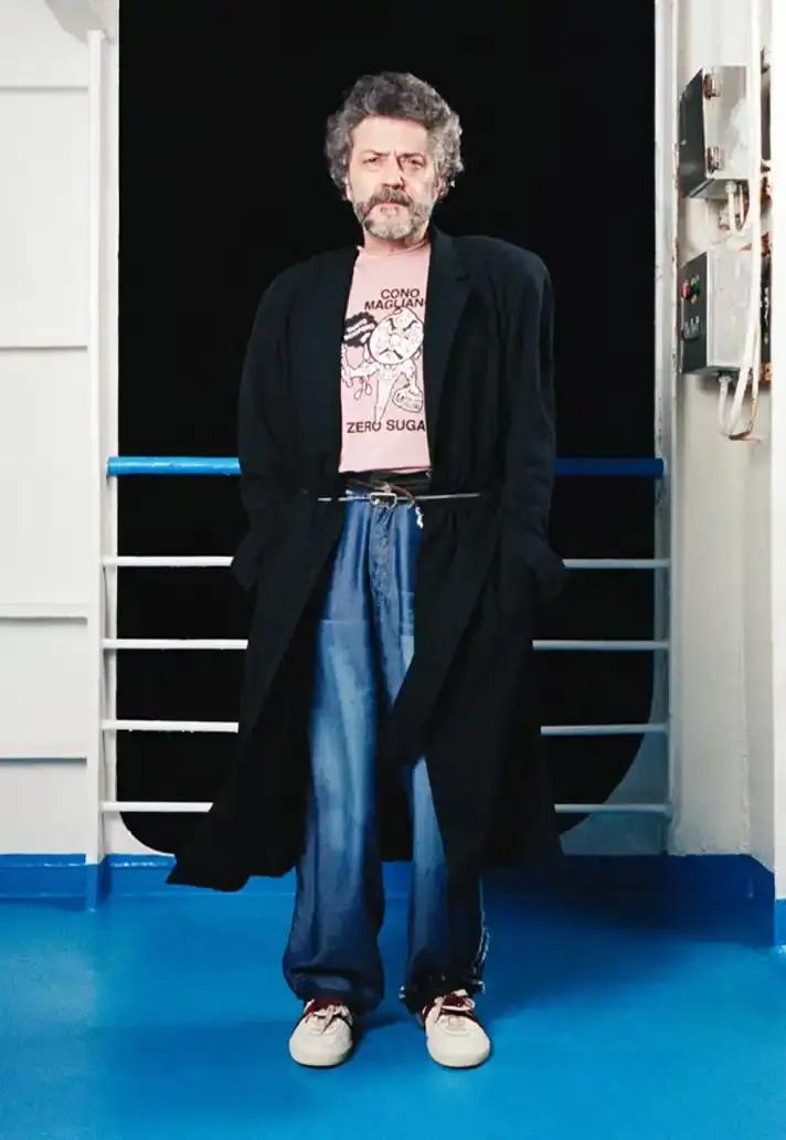 MAGLIANO SHOWS SS26 COLLECTION VIA FERRY FILM image about Italian designer Luca Magliano's Spring/Summer 2026 menswear collection, presented as a film aboard a ferry during Milan Fashion Week. The collection features camping and nomadic influences, with repurposed materials, loose silhouettes, and collaborative footwear including Beja soccer sneakers and 1900s-inspired boots. Shoot by Leonardo Scotti. (image 7 of 16)