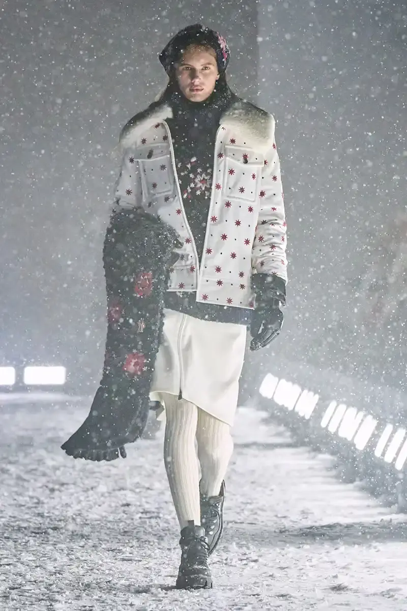 Moncler Moncler's Fall/Winter 2025 Grenoble collection showcase held at Courchevel Altiport in the French Alps. It details how the runway show transformed Europe's highest airport into a fashion venue at 2,008 meters above sea level. The article outlines the collection's 140 looks that blend urban style with mountain functionality, featuring innovative materials like denim and canvas alongside traditional winter textiles. It mentions the craftsmanship details including embroidery and intarsia patterns on ski suits. The article also notes celebrity attendees and a special snowboard collaboration with Shaun White's WHITESPACE brand. The content is organized in paragraphs describing the event setting, collection details, and notable highlights (image 22 of 22)