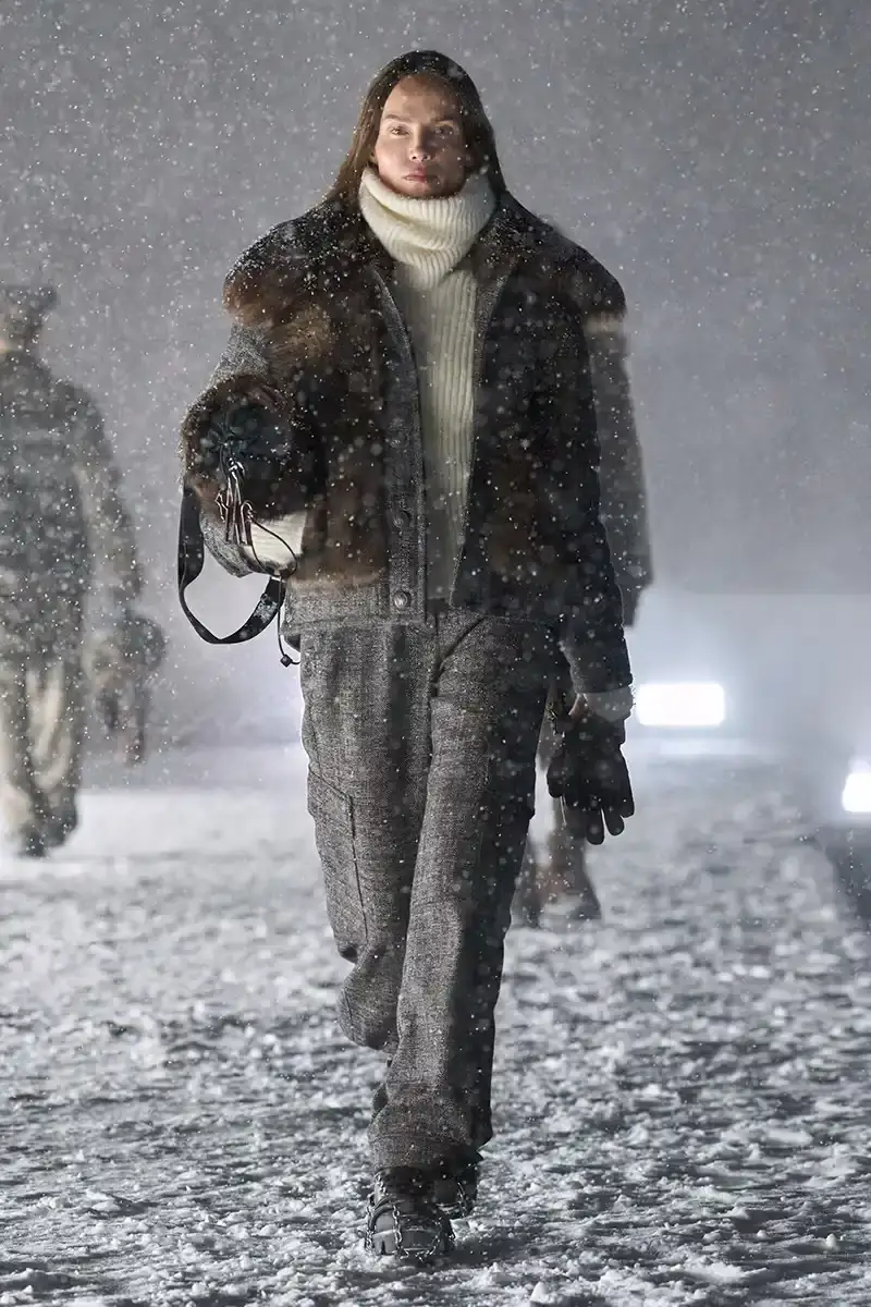 Moncler Moncler's Fall/Winter 2025 Grenoble collection showcase held at Courchevel Altiport in the French Alps. It details how the runway show transformed Europe's highest airport into a fashion venue at 2,008 meters above sea level. The article outlines the collection's 140 looks that blend urban style with mountain functionality, featuring innovative materials like denim and canvas alongside traditional winter textiles. It mentions the craftsmanship details including embroidery and intarsia patterns on ski suits. The article also notes celebrity attendees and a special snowboard collaboration with Shaun White's WHITESPACE brand. The content is organized in paragraphs describing the event setting, collection details, and notable highlights (image 15 of 22)