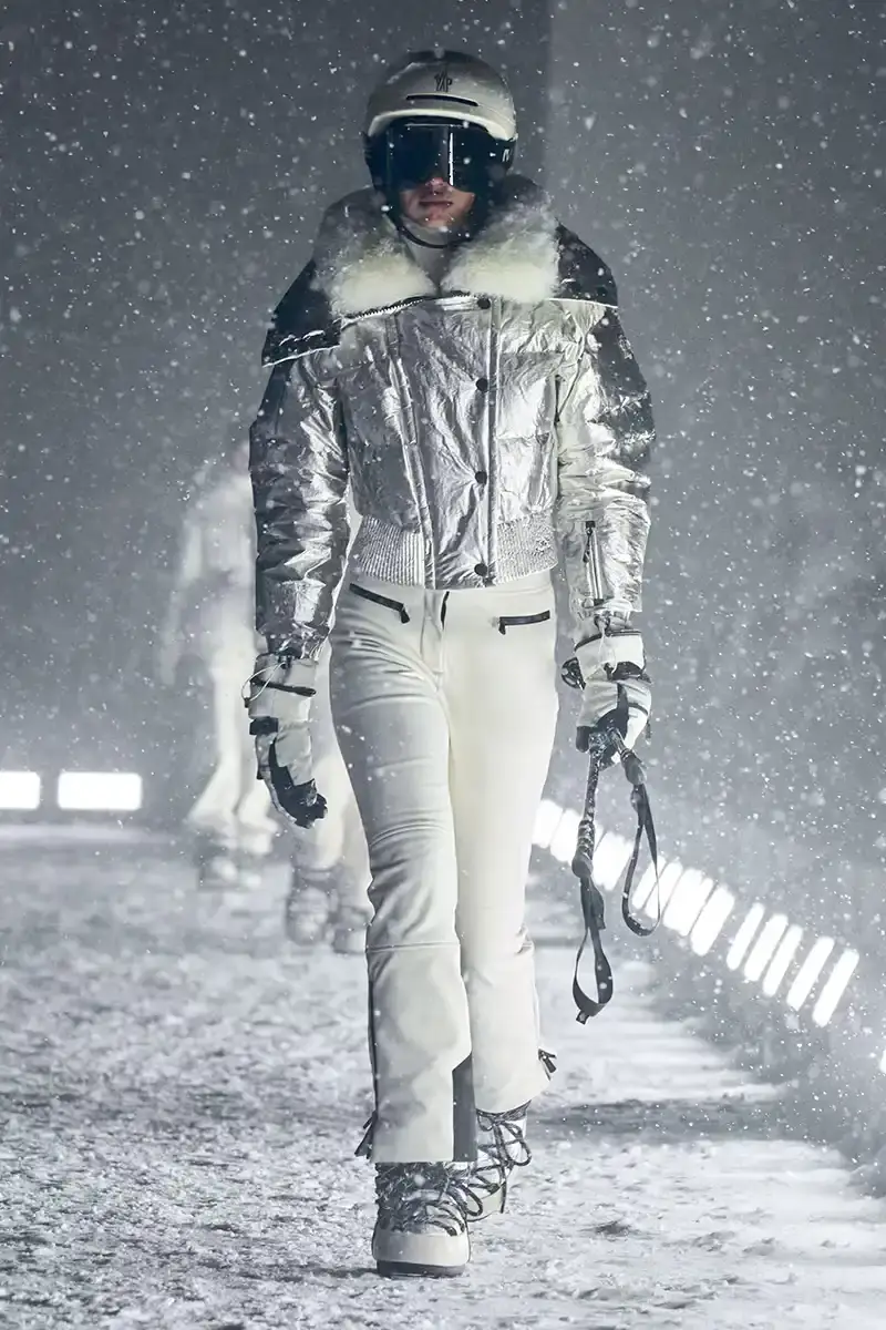 Moncler Moncler's Fall/Winter 2025 Grenoble collection showcase held at Courchevel Altiport in the French Alps. It details how the runway show transformed Europe's highest airport into a fashion venue at 2,008 meters above sea level. The article outlines the collection's 140 looks that blend urban style with mountain functionality, featuring innovative materials like denim and canvas alongside traditional winter textiles. It mentions the craftsmanship details including embroidery and intarsia patterns on ski suits. The article also notes celebrity attendees and a special snowboard collaboration with Shaun White's WHITESPACE brand. The content is organized in paragraphs describing the event setting, collection details, and notable highlights (image 14 of 22)
