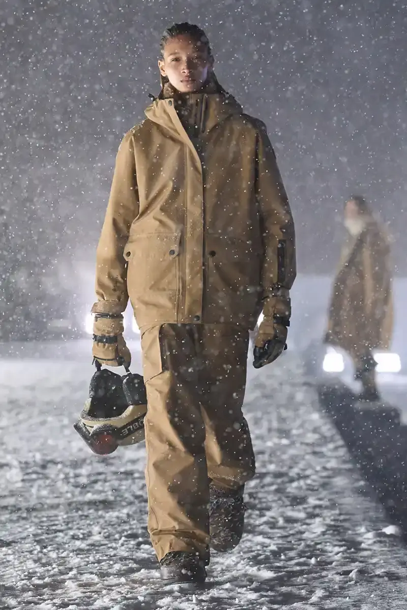 Moncler Moncler's Fall/Winter 2025 Grenoble collection showcase held at Courchevel Altiport in the French Alps. It details how the runway show transformed Europe's highest airport into a fashion venue at 2,008 meters above sea level. The article outlines the collection's 140 looks that blend urban style with mountain functionality, featuring innovative materials like denim and canvas alongside traditional winter textiles. It mentions the craftsmanship details including embroidery and intarsia patterns on ski suits. The article also notes celebrity attendees and a special snowboard collaboration with Shaun White's WHITESPACE brand. The content is organized in paragraphs describing the event setting, collection details, and notable highlights (image 8 of 22)