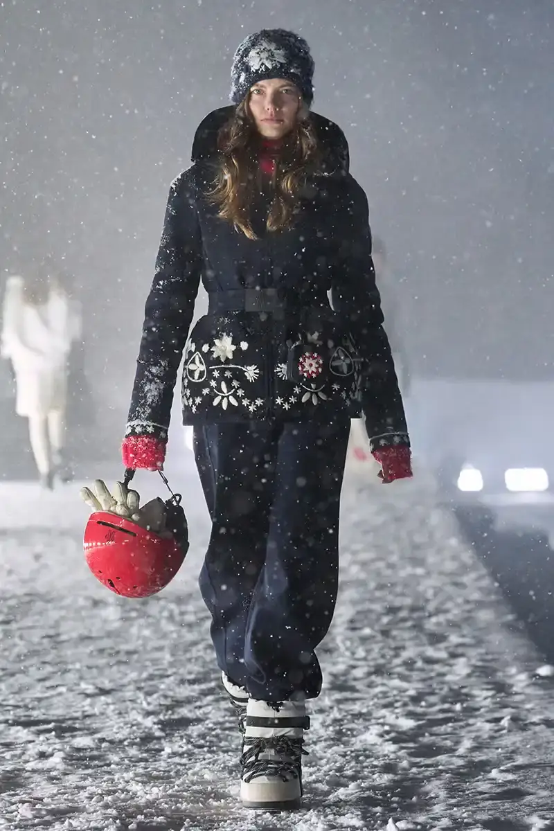 Moncler Moncler's Fall/Winter 2025 Grenoble collection showcase held at Courchevel Altiport in the French Alps. It details how the runway show transformed Europe's highest airport into a fashion venue at 2,008 meters above sea level. The article outlines the collection's 140 looks that blend urban style with mountain functionality, featuring innovative materials like denim and canvas alongside traditional winter textiles. It mentions the craftsmanship details including embroidery and intarsia patterns on ski suits. The article also notes celebrity attendees and a special snowboard collaboration with Shaun White's WHITESPACE brand. The content is organized in paragraphs describing the event setting, collection details, and notable highlights (image 20 of 22)