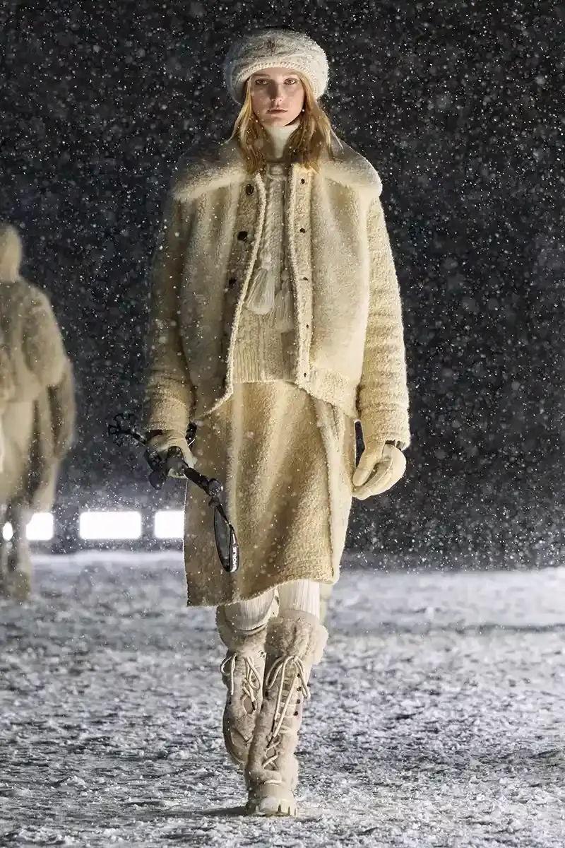 Moncler Moncler's Fall/Winter 2025 Grenoble collection showcase held at Courchevel Altiport in the French Alps. It details how the runway show transformed Europe's highest airport into a fashion venue at 2,008 meters above sea level. The article outlines the collection's 140 looks that blend urban style with mountain functionality, featuring innovative materials like denim and canvas alongside traditional winter textiles. It mentions the craftsmanship details including embroidery and intarsia patterns on ski suits. The article also notes celebrity attendees and a special snowboard collaboration with Shaun White's WHITESPACE brand. The content is organized in paragraphs describing the event setting, collection details, and notable highlights (image 16 of 22)