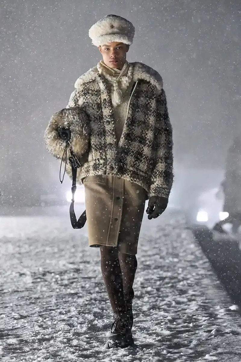 Moncler Moncler's Fall/Winter 2025 Grenoble collection showcase held at Courchevel Altiport in the French Alps. It details how the runway show transformed Europe's highest airport into a fashion venue at 2,008 meters above sea level. The article outlines the collection's 140 looks that blend urban style with mountain functionality, featuring innovative materials like denim and canvas alongside traditional winter textiles. It mentions the craftsmanship details including embroidery and intarsia patterns on ski suits. The article also notes celebrity attendees and a special snowboard collaboration with Shaun White's WHITESPACE brand. The content is organized in paragraphs describing the event setting, collection details, and notable highlights (image 11 of 22)