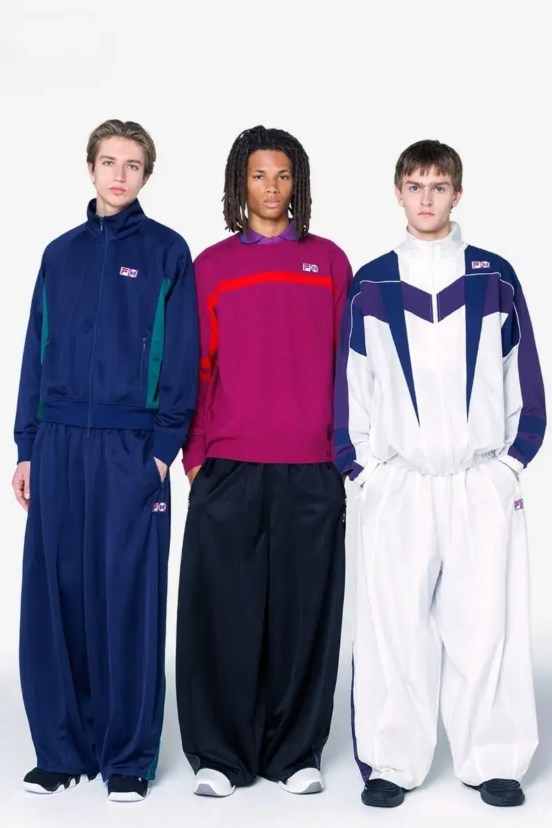NEEDLES AND FILA RELEASE FW26 CAPSULE Two fashion models present sportswear from the NEEDLES and FILA FW26 collection in teal, navy, and magenta against a neutral studio backdrop. (image 2 of 12)