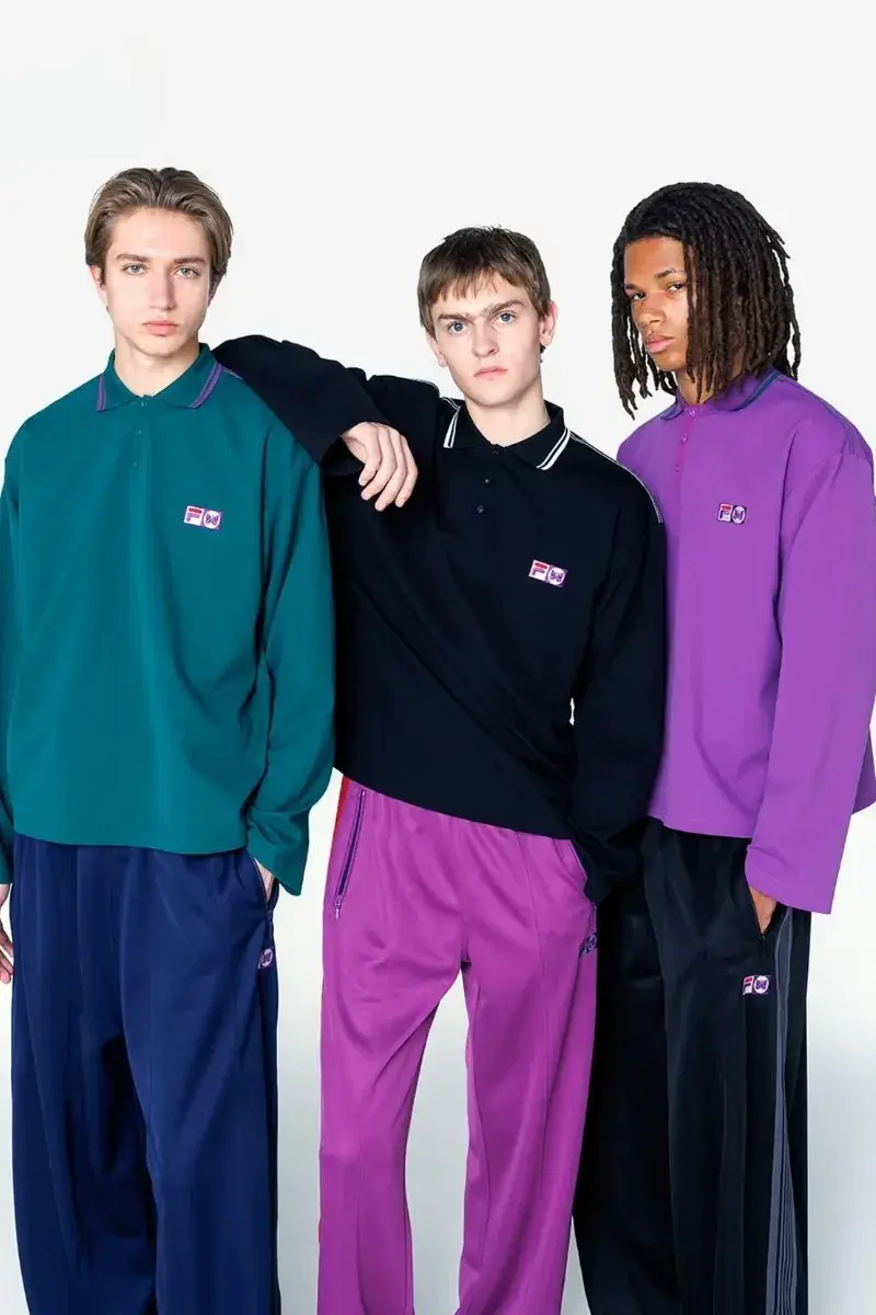NEEDLES AND FILA RELEASE FW26 CAPSULE Two fashion models present sportswear from the NEEDLES and FILA FW26 collection in teal, navy, and magenta against a neutral studio backdrop. (image 11 of 12)