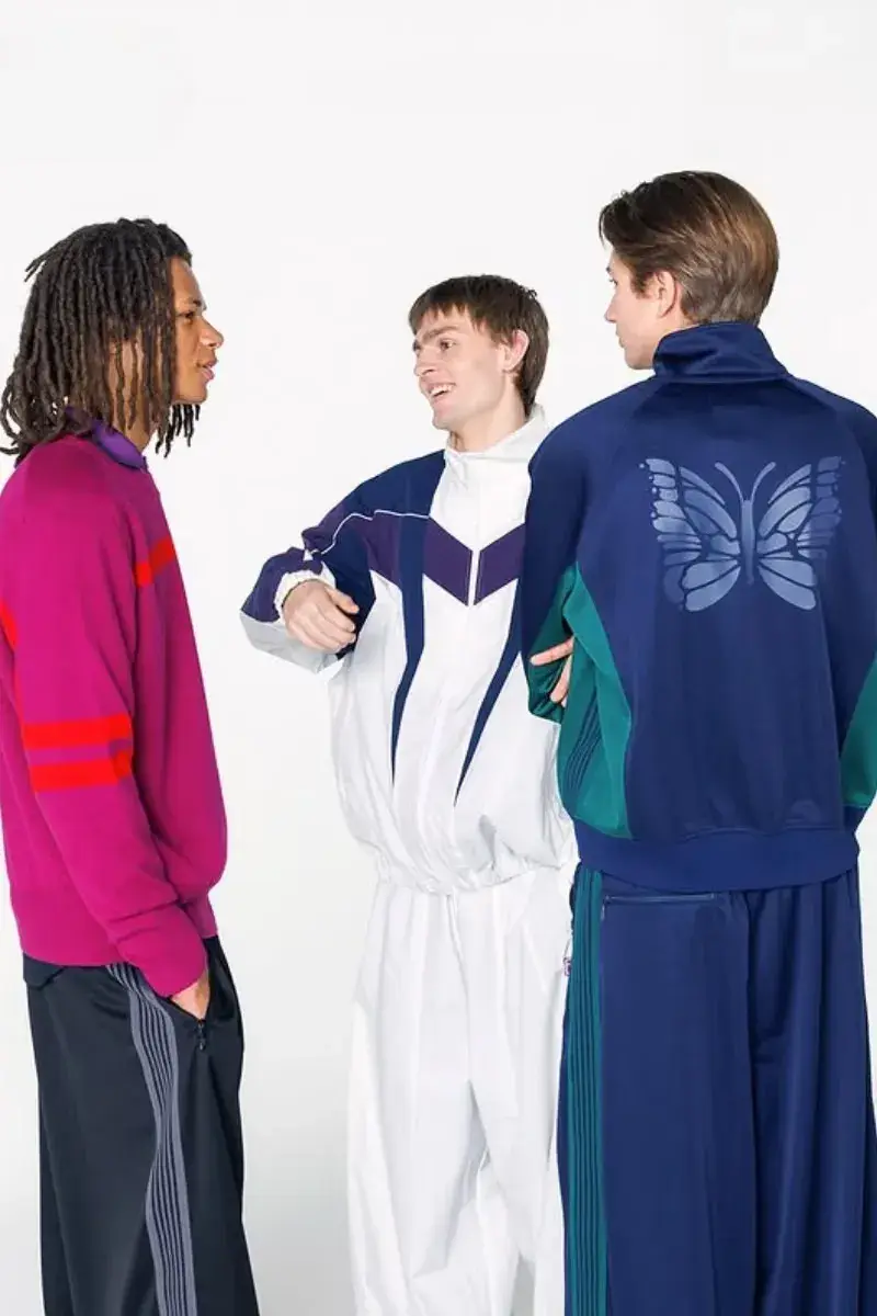 NEEDLES AND FILA RELEASE FW26 CAPSULE Two fashion models present sportswear from the NEEDLES and FILA FW26 collection in teal, navy, and magenta against a neutral studio backdrop.