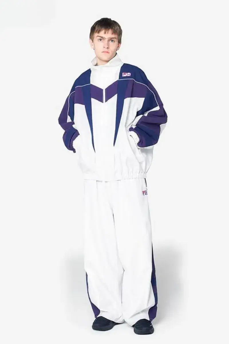 NEEDLES AND FILA RELEASE FW26 CAPSULE Two fashion models present sportswear from the NEEDLES and FILA FW26 collection in teal, navy, and magenta against a neutral studio backdrop. (image 3 of 12)
