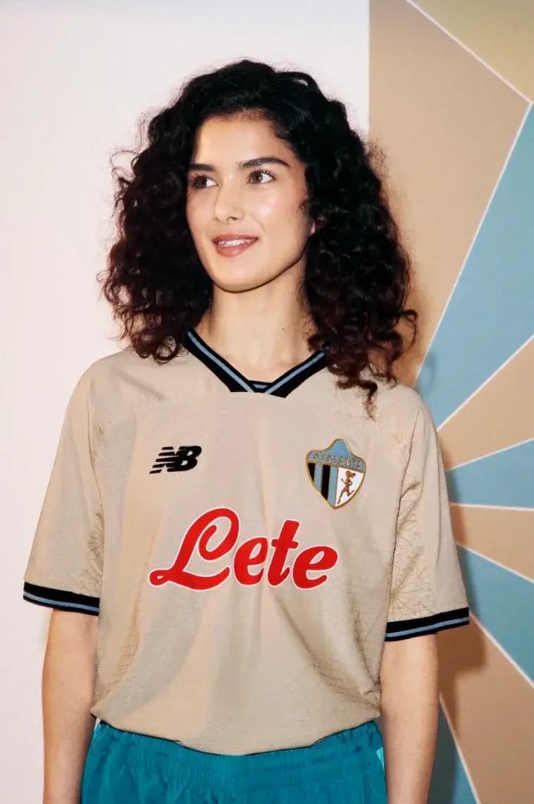 NEW BALANCE ATALANTA BC 2026/27 THIRD KIT image of A beige Atalanta BC football shirt with black and blue trim, featuring a gold 1964 logo and a geometric jacquard pattern.