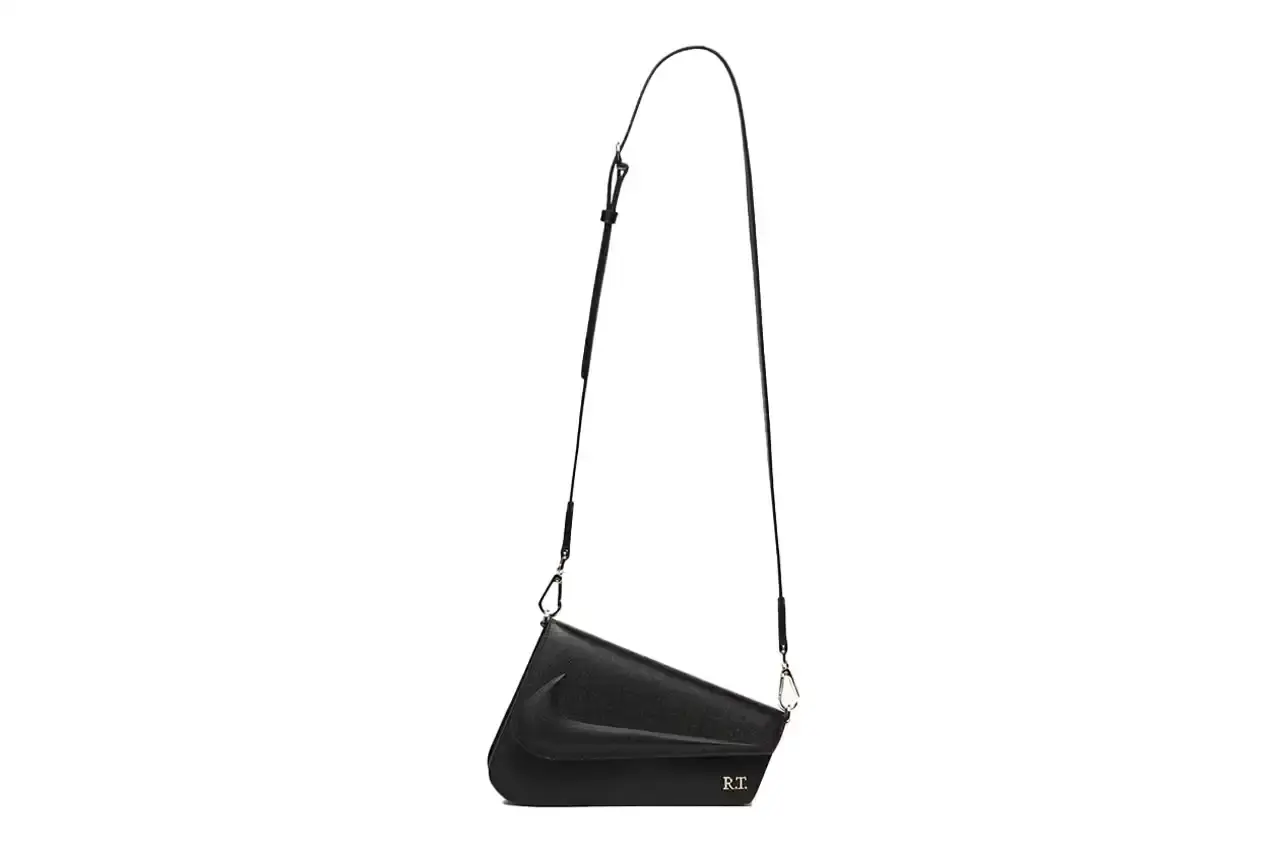 Nike x Riccardo Tisci The Mercer Bag by Nike x Riccardo Tisci, shown in black pebbled leather with gold hardware. The minimalist design features a front flap with debossed Nike logo and R.T. metal signature at the corner. The bag includes an adjustable shoulder strap. (image 3 of 6)