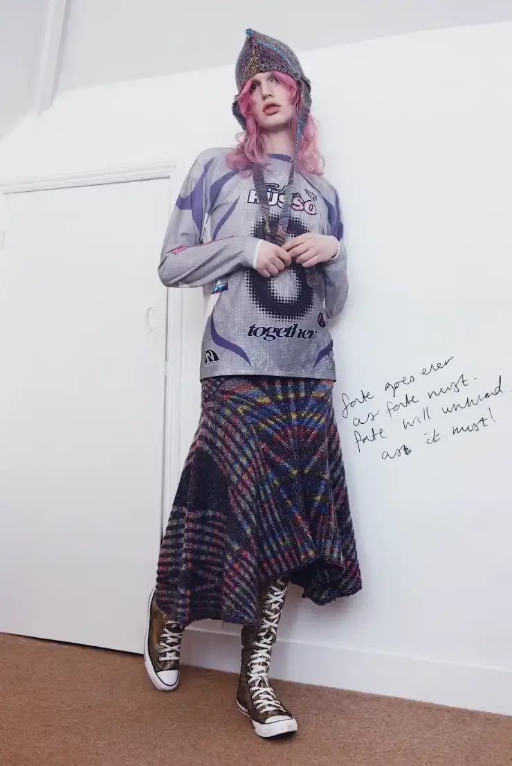 PAOLINA RUSSO'S AUTUMN-WINTER LINE BLENDS MEDIEVAL AND Y2K Photo of Paolina Russo's Autumn-Winter 2025 fashion collection, which combines medieval tailoring with early 2010s aesthetics. The collection features purple as a dominant color across various pieces, including denim, hoodies, and knits. Key elements include evolved "warrior knit" pieces, gold foil embellishments, and practical accessories like detachable hoods. The article also describes the designers' approach to merging traditional craftsmanship with modern technology, and mentions their recent industry recognitions including Forbes 30 under 30 and being finalists for prestigious fashion prizes.