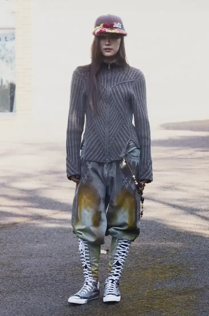 PAOLINA RUSSO'S AUTUMN-WINTER LINE BLENDS MEDIEVAL AND Y2K Photo of Paolina Russo's Autumn-Winter 2025 fashion collection, which combines medieval tailoring with early 2010s aesthetics. The collection features purple as a dominant color across various pieces, including denim, hoodies, and knits. Key elements include evolved "warrior knit" pieces, gold foil embellishments, and practical accessories like detachable hoods. The article also describes the designers' approach to merging traditional craftsmanship with modern technology, and mentions their recent industry recognitions including Forbes 30 under 30 and being finalists for prestigious fashion prizes. (image 2 of 12)