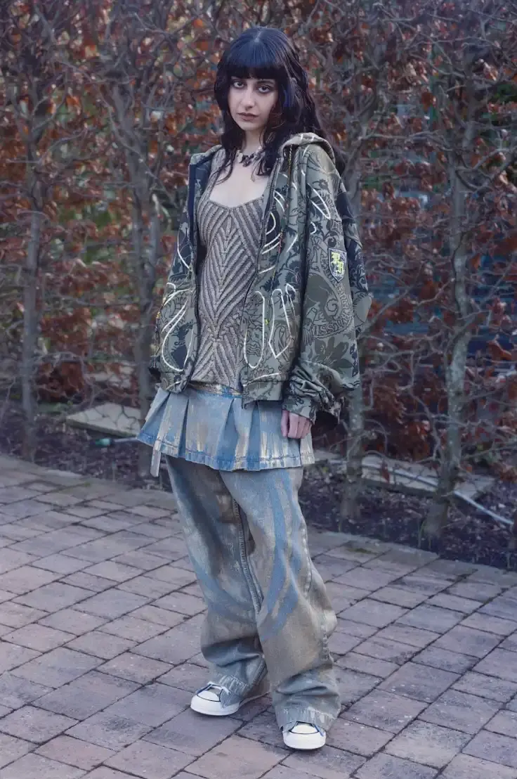 PAOLINA RUSSO'S AUTUMN-WINTER LINE BLENDS MEDIEVAL AND Y2K Photo of Paolina Russo's Autumn-Winter 2025 fashion collection, which combines medieval tailoring with early 2010s aesthetics. The collection features purple as a dominant color across various pieces, including denim, hoodies, and knits. Key elements include evolved "warrior knit" pieces, gold foil embellishments, and practical accessories like detachable hoods. The article also describes the designers' approach to merging traditional craftsmanship with modern technology, and mentions their recent industry recognitions including Forbes 30 under 30 and being finalists for prestigious fashion prizes. (image 4 of 12)