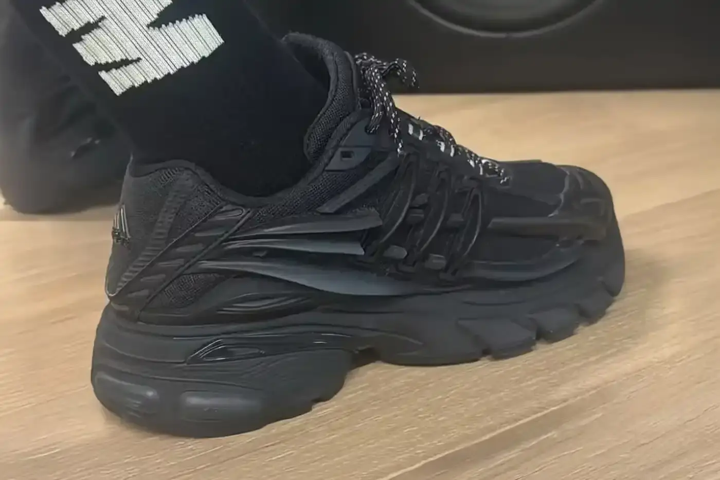 An image of the Pharrell x adidas Jellyfish sneaker in a complete black colorway. The shoe features distinctive plastic overlays, an adiPRENE midsole, and reflective details on the eyelets and laces. Design highlights include a potential jellyfish logo and Virginia branding on the tongue.
