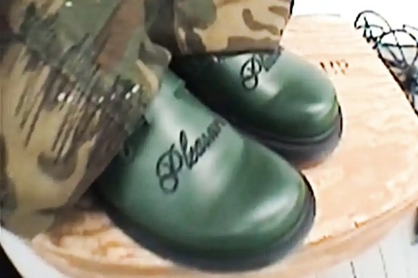 Ian Dooley/Pleasures Green leather Dr. Martens Jorge Mule featuring black metal buckles, cursive PLEASURES branding stitched on the upper, signature yellow stitching, and a black Vibram outsole. The collaboration merges both brands' distinctive styles in a versatile slip-on design.