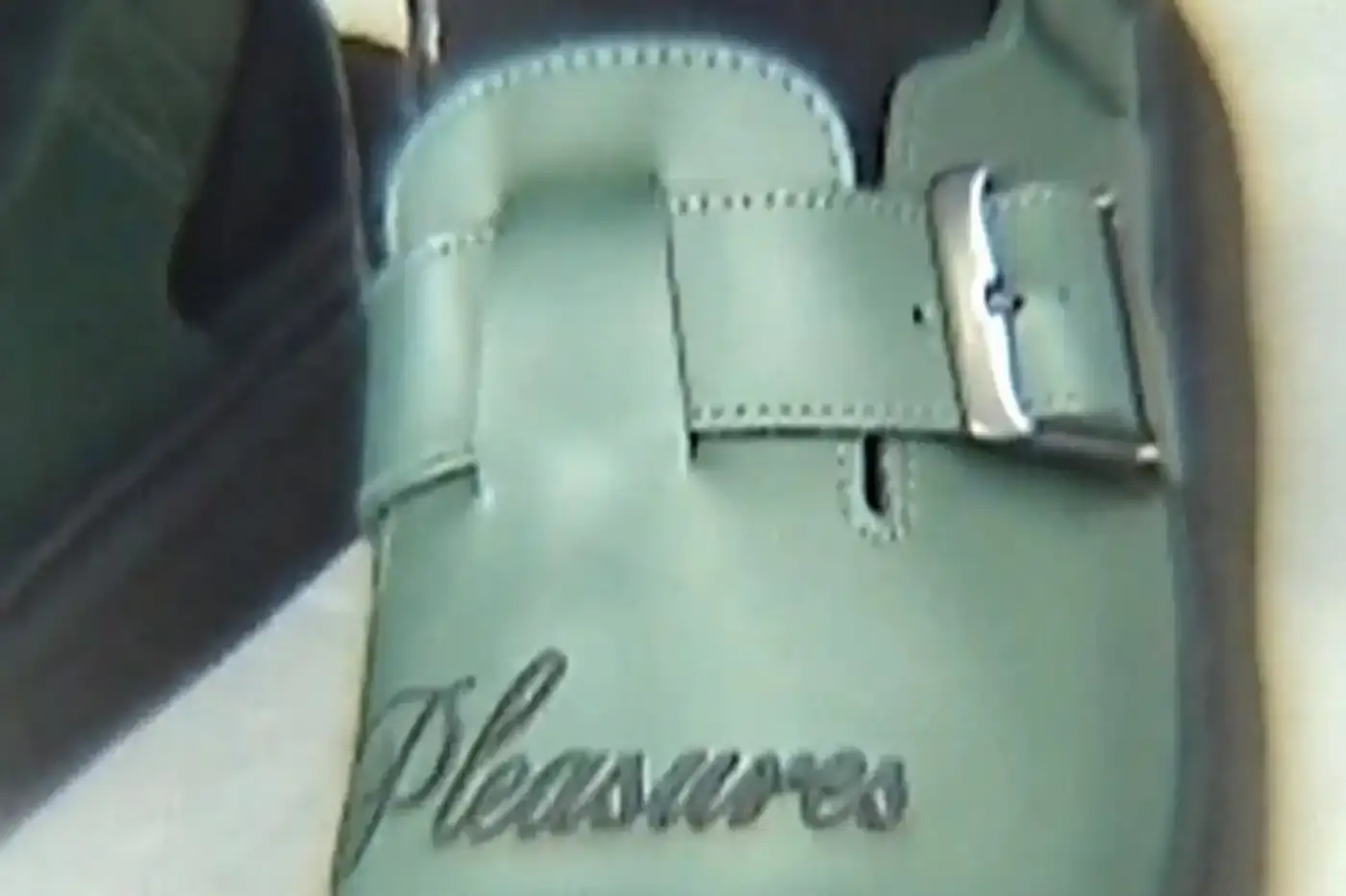 Ian Dooley/Pleasures Green leather Dr. Martens Jorge Mule featuring black metal buckles, cursive PLEASURES branding stitched on the upper, signature yellow stitching, and a black Vibram outsole. The collaboration merges both brands' distinctive styles in a versatile slip-on design. (image 2 of 11)