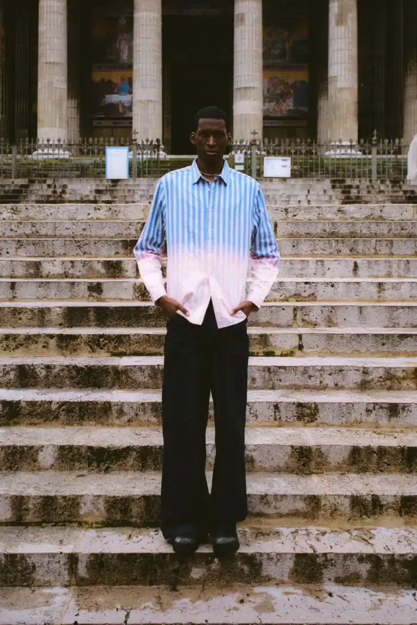 Quinn Dunziellas PLEASURES Spring/Summer 2025 lookbook photograph showcases models wearing the new collection against Parisian backdrops. Featured items include a Realtree camo jacket, leopard print blazer, and holographic-lined outerwear pieces. (image 4 of 15)