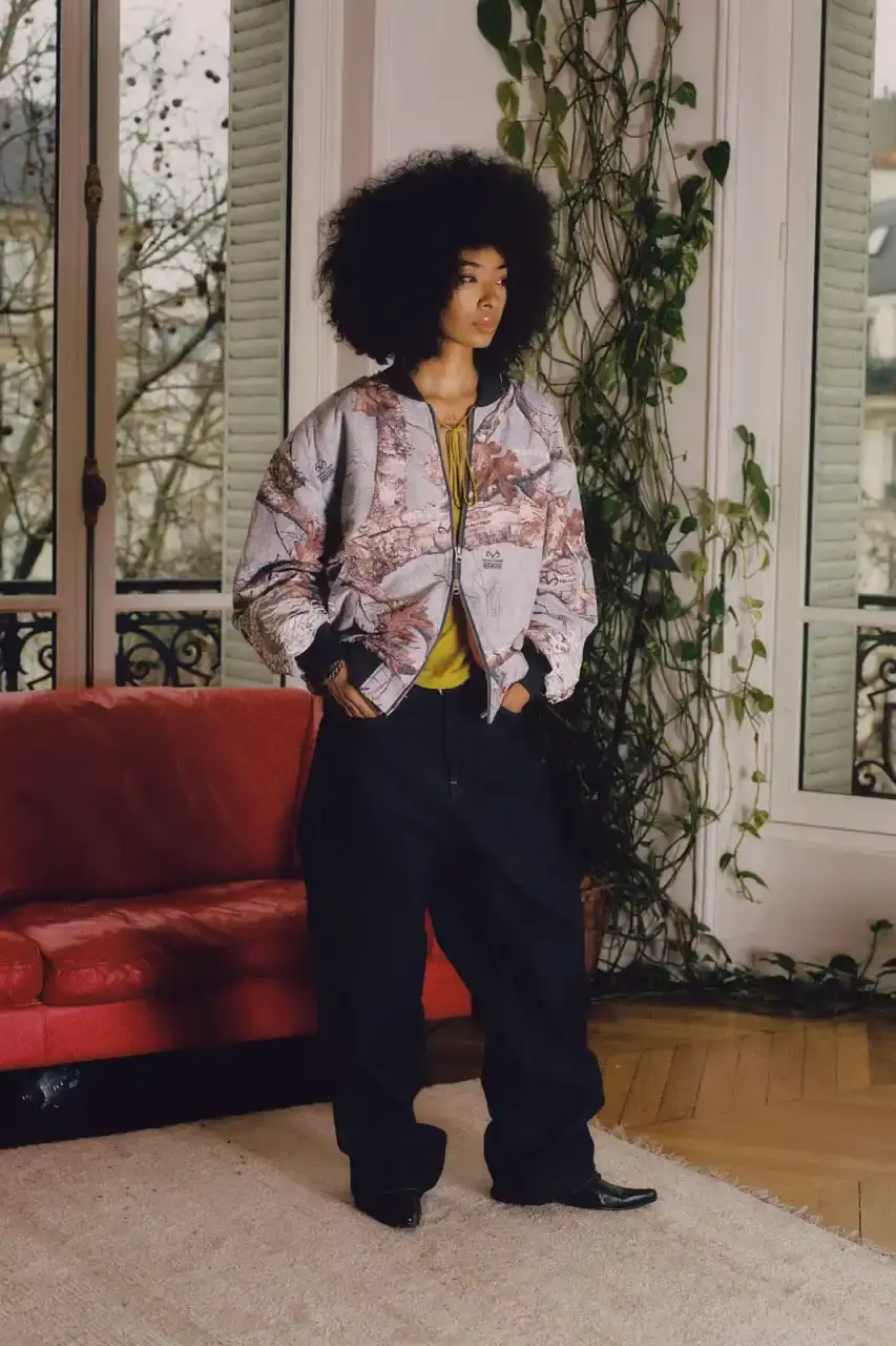 Quinn Dunziellas PLEASURES Spring/Summer 2025 lookbook photograph showcases models wearing the new collection against Parisian backdrops. Featured items include a Realtree camo jacket, leopard print blazer, and holographic-lined outerwear pieces. (image 10 of 15)