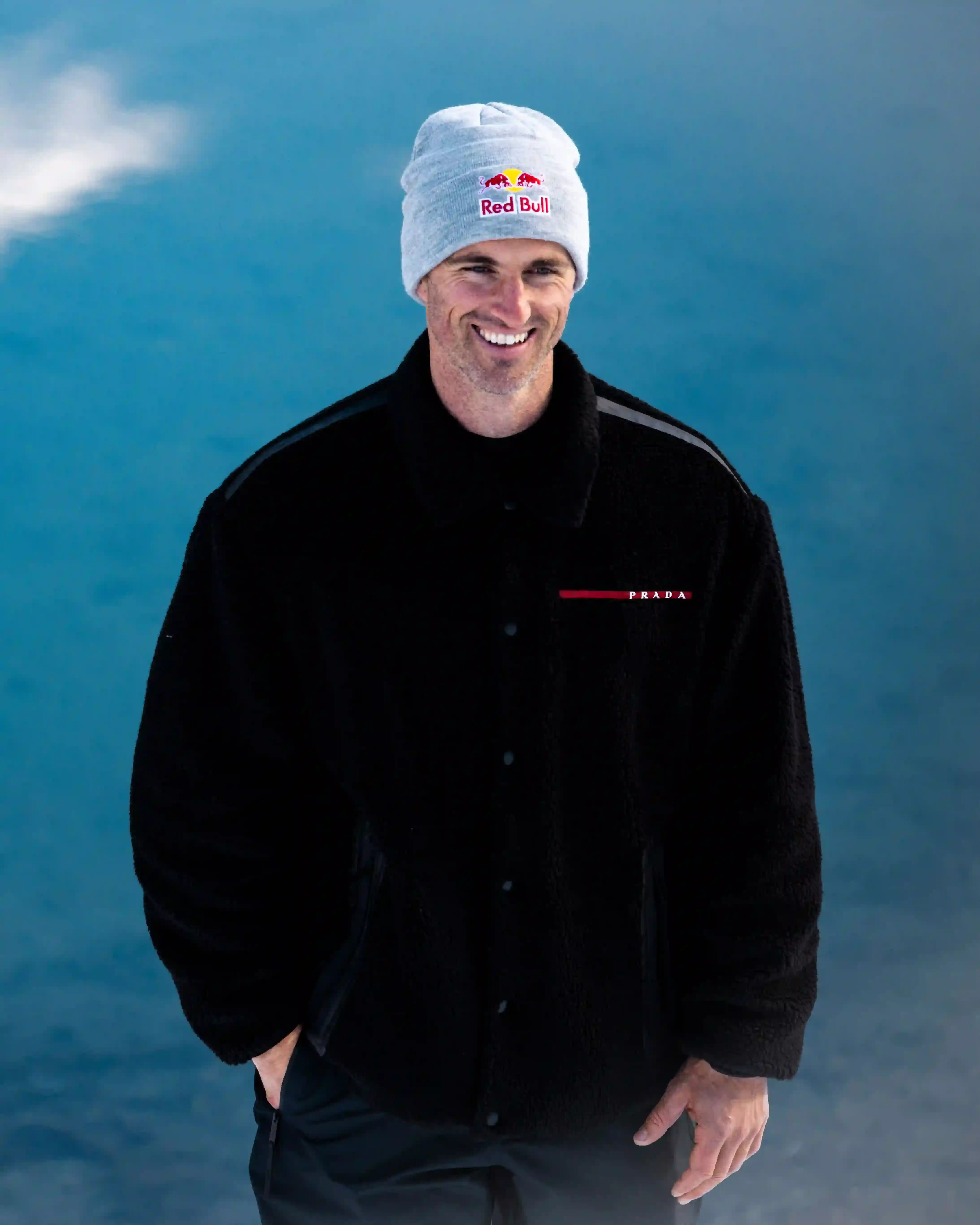 Prada Linea Rossa Snowboarder Pierre Vaultier riding on a narrow 50-centimeter track over a partially frozen lake in Serre-Chevalier. He wears black and red Prada Linea Rossa technical gear against a backdrop of snow-covered French Alps. (image 4 of 4)