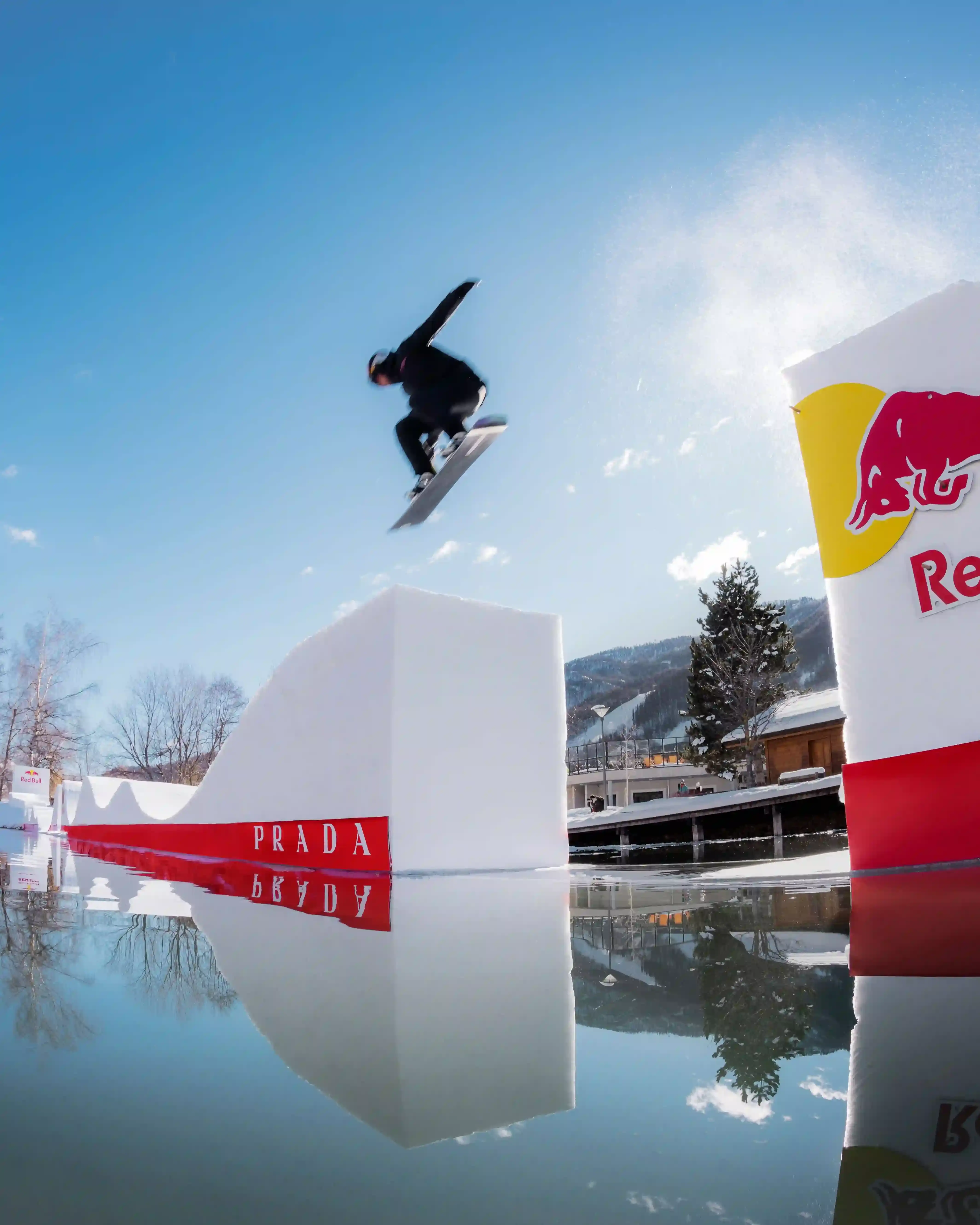 Prada Linea Rossa Snowboarder Pierre Vaultier riding on a narrow 50-centimeter track over a partially frozen lake in Serre-Chevalier. He wears black and red Prada Linea Rossa technical gear against a backdrop of snow-covered French Alps. (image 1 of 4)