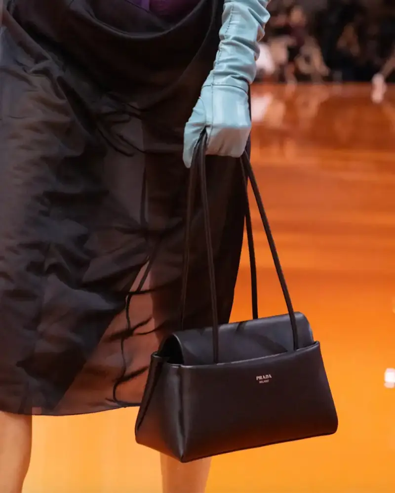PRADA PASSAGE: THE TRAPEZOID BAG FROM SPRING/SUMMER 2026 image about Prada's new Passage bag from the Spring/Summer 2026 collection, featuring a trapezoid shape, three pockets, and black leather construction. (image 2 of 6)