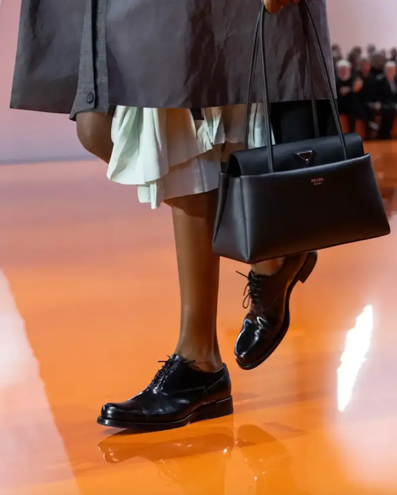 PRADA PASSAGE: THE TRAPEZOID BAG FROM SPRING/SUMMER 2026 image about Prada's new Passage bag from the Spring/Summer 2026 collection, featuring a trapezoid shape, three pockets, and black leather construction. (image 4 of 6)
