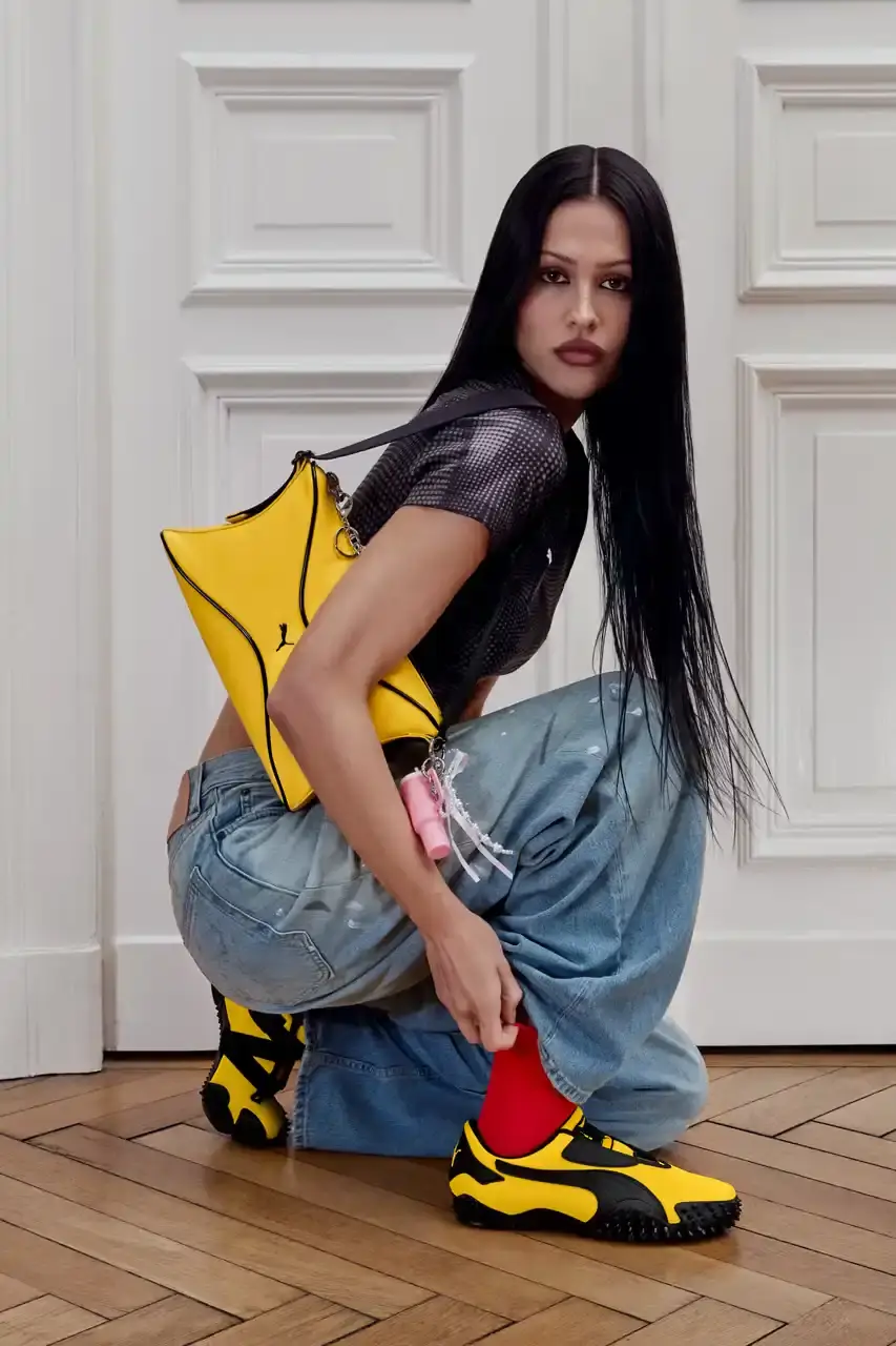 PUMA MOSTRO RETURNS IN PELÉ YELLOW WITH AMELIA GRAY image of PUMA's latest Mostro sneaker release in yellow colorway, featuring model Amelia Gray in promotional campaign imagery. Includes product specifications, pricing at $120 USD, and June 5 release date through PUMA retail channels. (image 4 of 7)