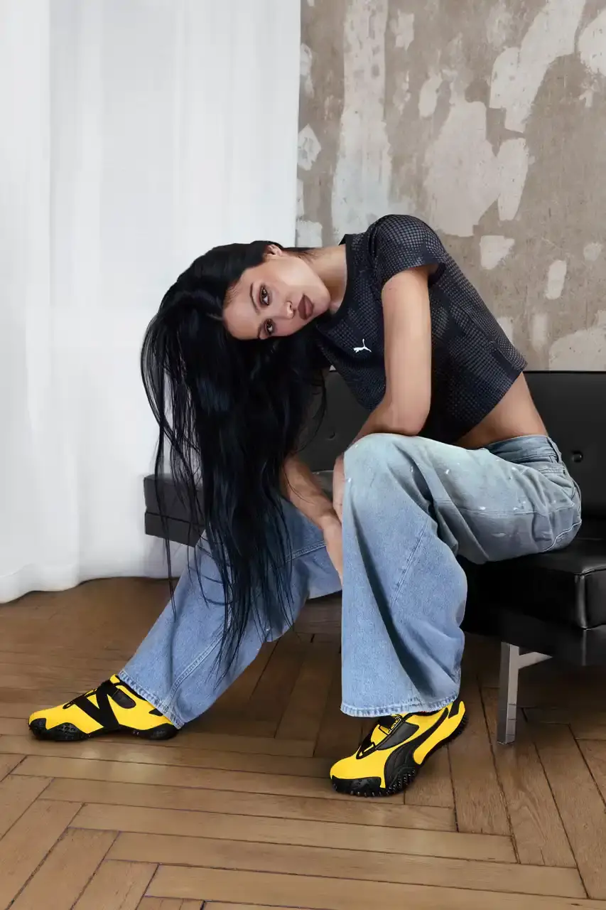 PUMA MOSTRO RETURNS IN PELÉ YELLOW WITH AMELIA GRAY image of PUMA's latest Mostro sneaker release in yellow colorway, featuring model Amelia Gray in promotional campaign imagery. Includes product specifications, pricing at $120 USD, and June 5 release date through PUMA retail channels.