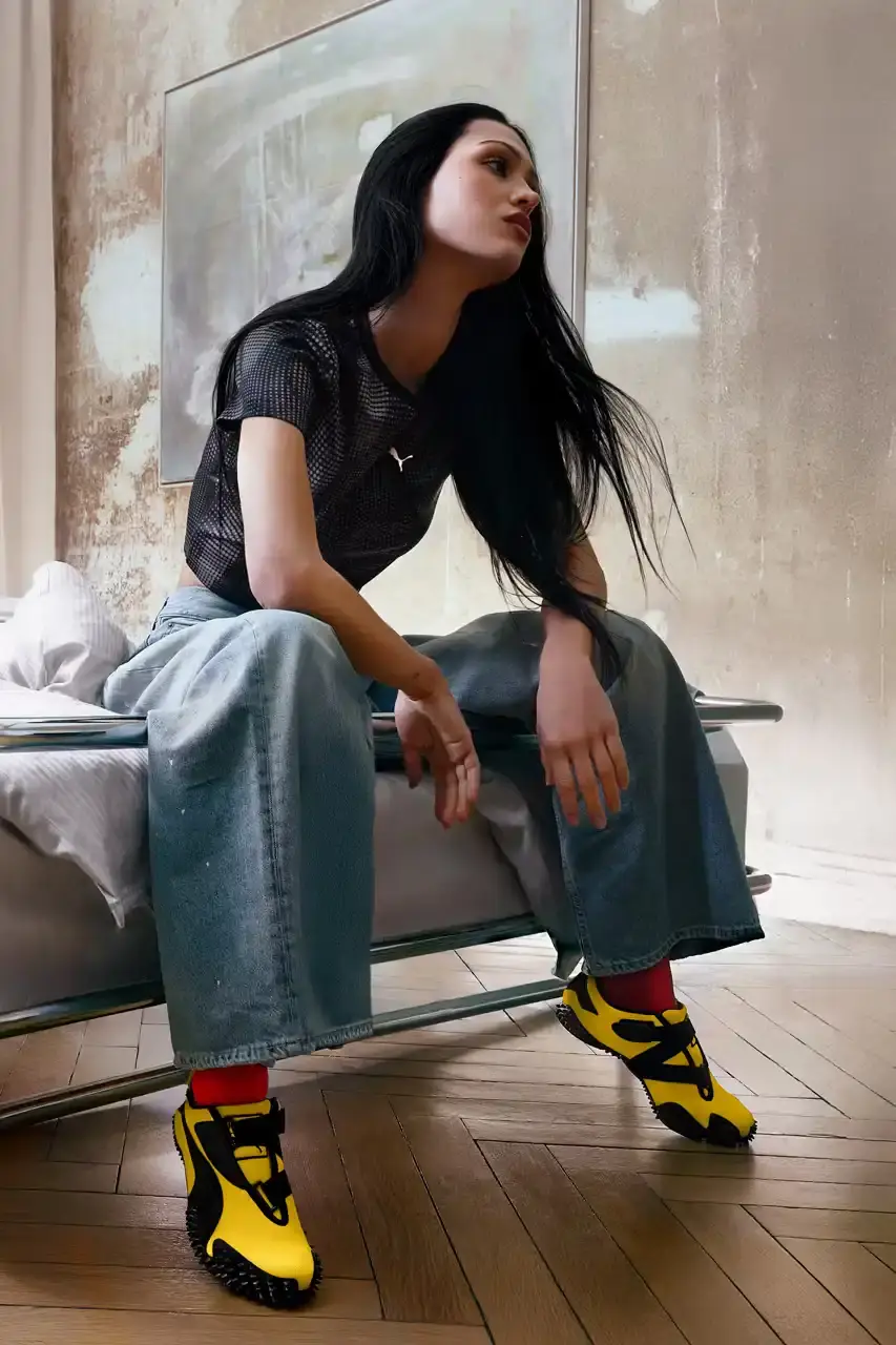 PUMA MOSTRO RETURNS IN PELÉ YELLOW WITH AMELIA GRAY image of PUMA's latest Mostro sneaker release in yellow colorway, featuring model Amelia Gray in promotional campaign imagery. Includes product specifications, pricing at $120 USD, and June 5 release date through PUMA retail channels. (image 6 of 7)