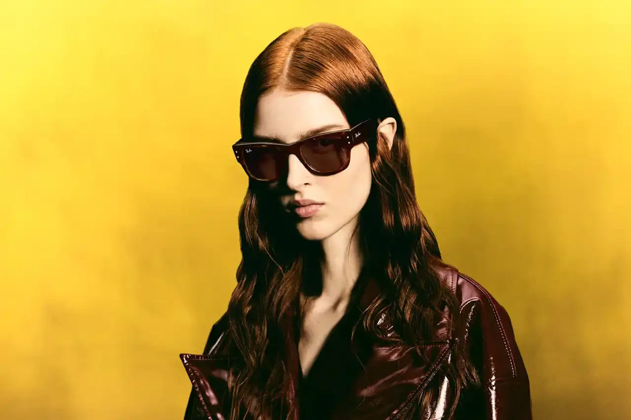 RAY-BAN UPDATES CLASSIC FRAMES WITH MODERN TWISTS photo of Ray-Ban's updates to two classic eyewear designs. It covers how the 95-year-old company has refreshed the Balorama frame (originally from 1967) with enhanced structural elements while maintaining its distinctive wraparound profile. The article also describes the new Mega Wayfarer variation, which keeps the signature square silhouette but introduces wider temples and thicker rims. The piece mentions Ray-Ban's history of design innovation and cultural relevance, noting how these updated classics honor their original character while incorporating modern features. (image 4 of 6)