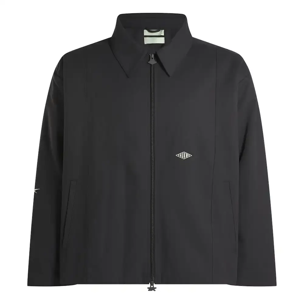 Reebok Tobe Nwigwe wearing a mint green coach jacket and black pants from the Reebok x Chukwu collection, standing next to the Chukwu OTU sneaker (image 8 of 9)