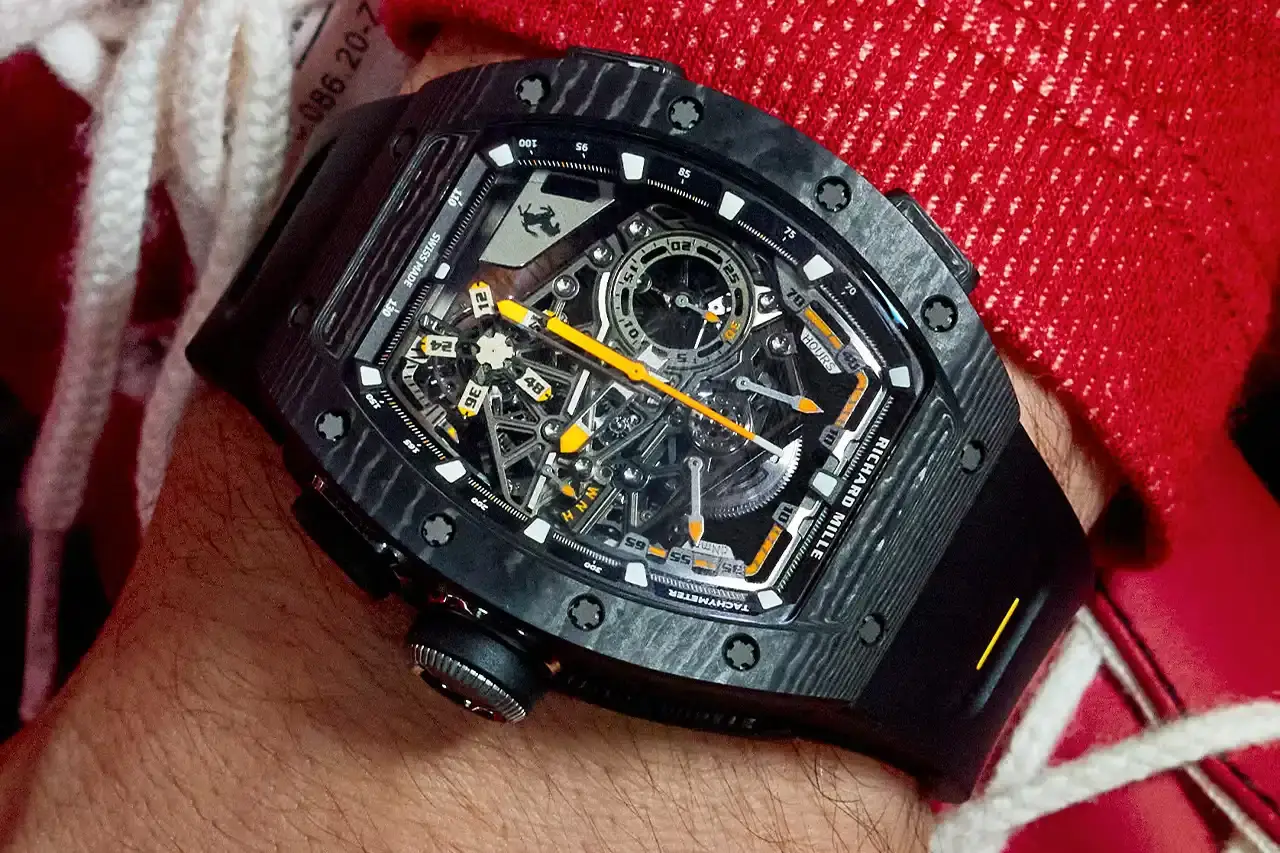 PRECISION MECHANICS: RICHARD MILLE'S FERRARI TRIBUTE WATCH A collaborative watch between Richard Mille and Ferrari, highlighting its design, technological features, and automotive-inspired elements. The text provides a comprehensive overview of the RM 43-01 Tourbillon Split-Seconds Chronograph, detailing its mechanical specifications, design influences from Ferrari's Centro Stile, and limited edition variants. The description covers technical aspects such as power reserve, movement design, and aesthetic connections to Ferrari's automotive heritage, making the complex watch design accessible to readers with varying levels of horological expertise. (image 6 of 7)