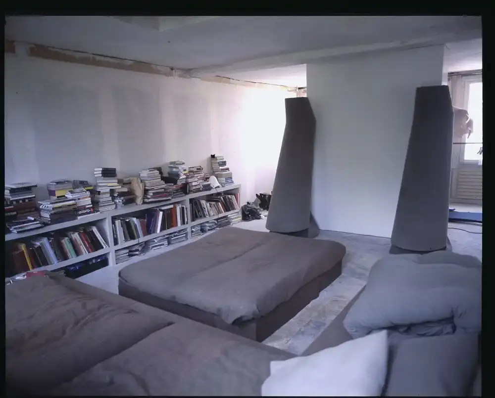 Assaf Shoshan/PIN–UP Interior of Rick Owens' brutalist Parisian home featuring unpolished floors, exposed wiring, a platform bed with Swiss Army blankets, and minimalist furnishings. (image 4 of 6)