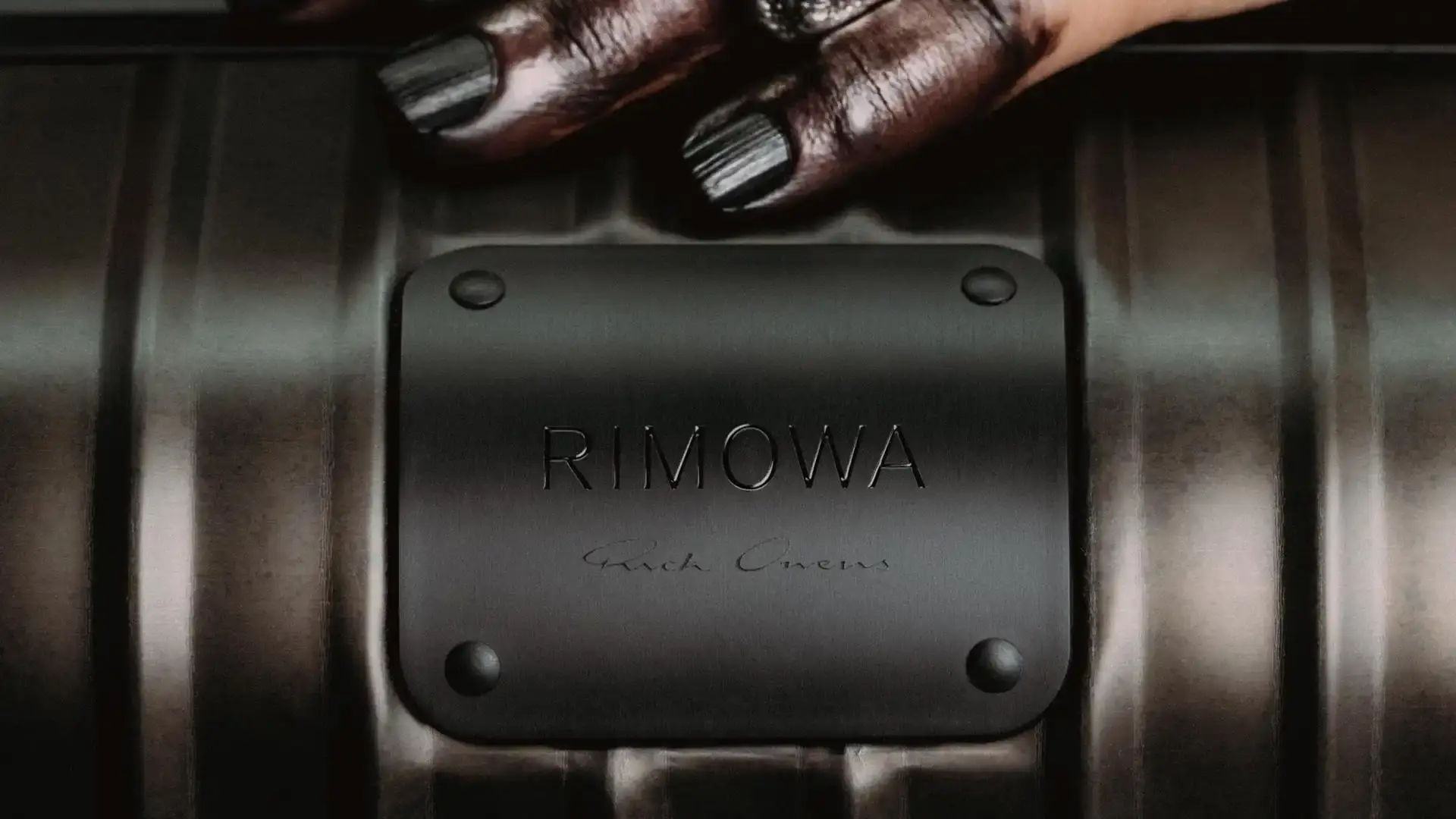 RIMOWA x Rick Owens bronze aluminum cabin suitcase with dark metallic finish and black leather details against neutral background