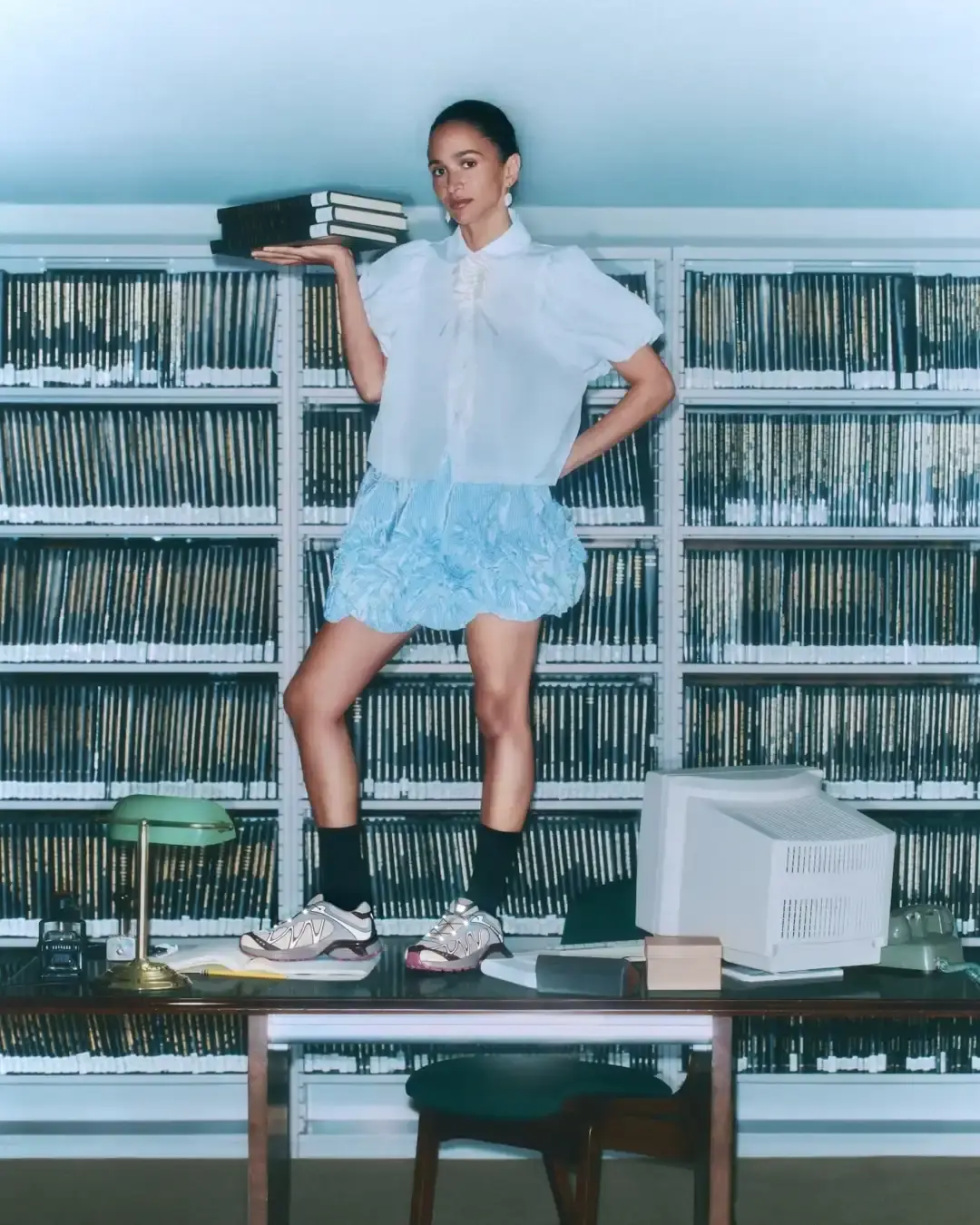 Salomon Three Gohar sisters—Laila, Nadia, and Janna—seated in a New York library wearing SALOMON XT-Whisper sneakers. They're arranged in stylish poses among bookshelves, demonstrating the shoe's elegant design in a quiet setting that reflects the "whisper" concept.