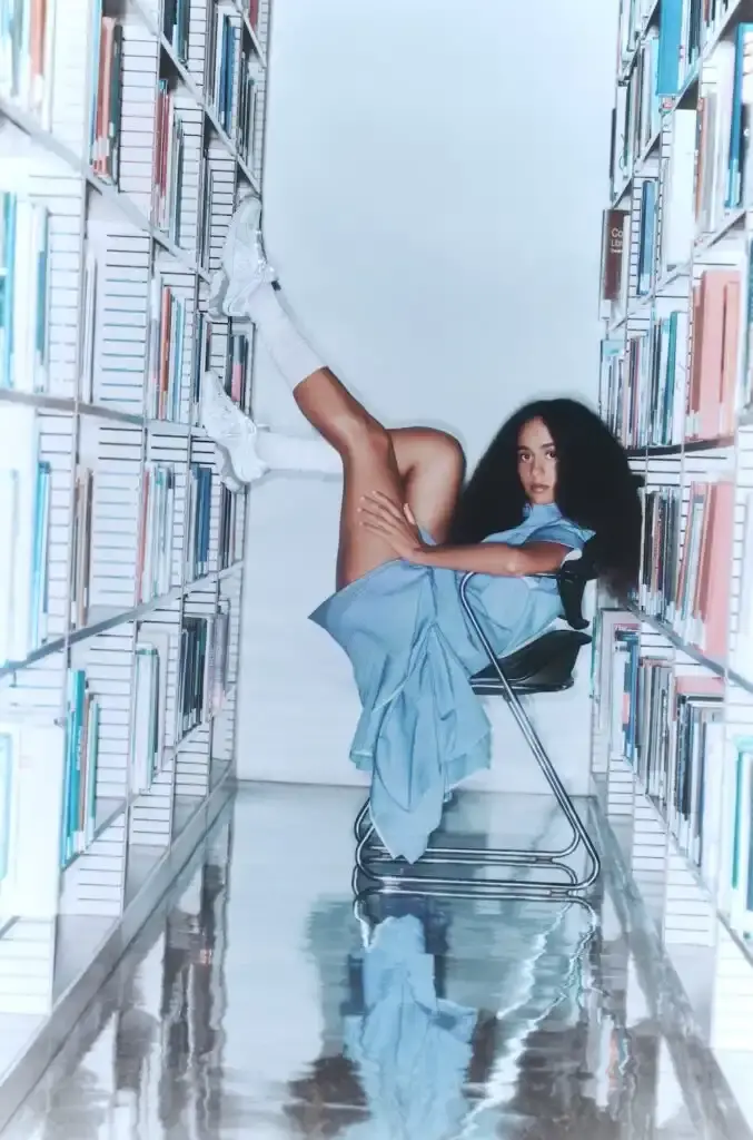Salomon Three Gohar sisters—Laila, Nadia, and Janna—seated in a New York library wearing SALOMON XT-Whisper sneakers. They're arranged in stylish poses among bookshelves, demonstrating the shoe's elegant design in a quiet setting that reflects the "whisper" concept. (image 2 of 5)