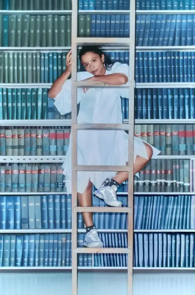 Salomon Three Gohar sisters—Laila, Nadia, and Janna—seated in a New York library wearing SALOMON XT-Whisper sneakers. They're arranged in stylish poses among bookshelves, demonstrating the shoe's elegant design in a quiet setting that reflects the "whisper" concept. (image 3 of 5)